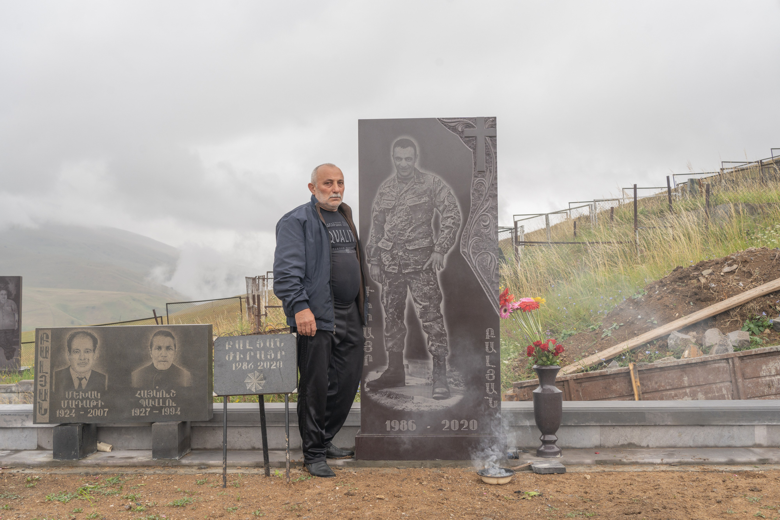 Levon Balyan is posing on the grave of his son who died during the 2020 Nagorno-Karabakh war. Levon is a farmer. Taking care of poultry and livestock helps him survive his son's passing. Otherwise, Levon says, it would have been impossible for him to grieve.