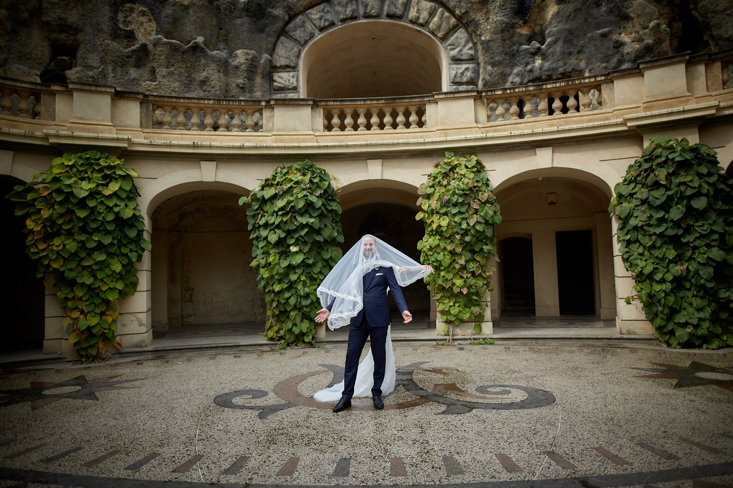 Bride playfully veiling groom in romantic Grebovka artificial cave Prague.