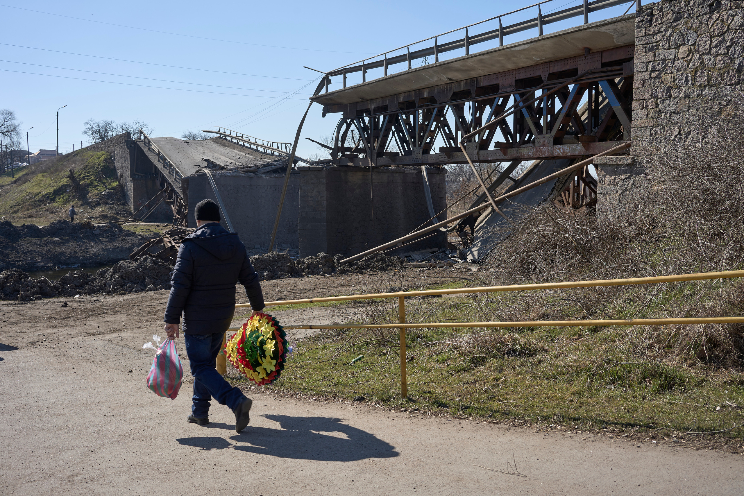 A man with funeral wreath passing by the demolished bridge.