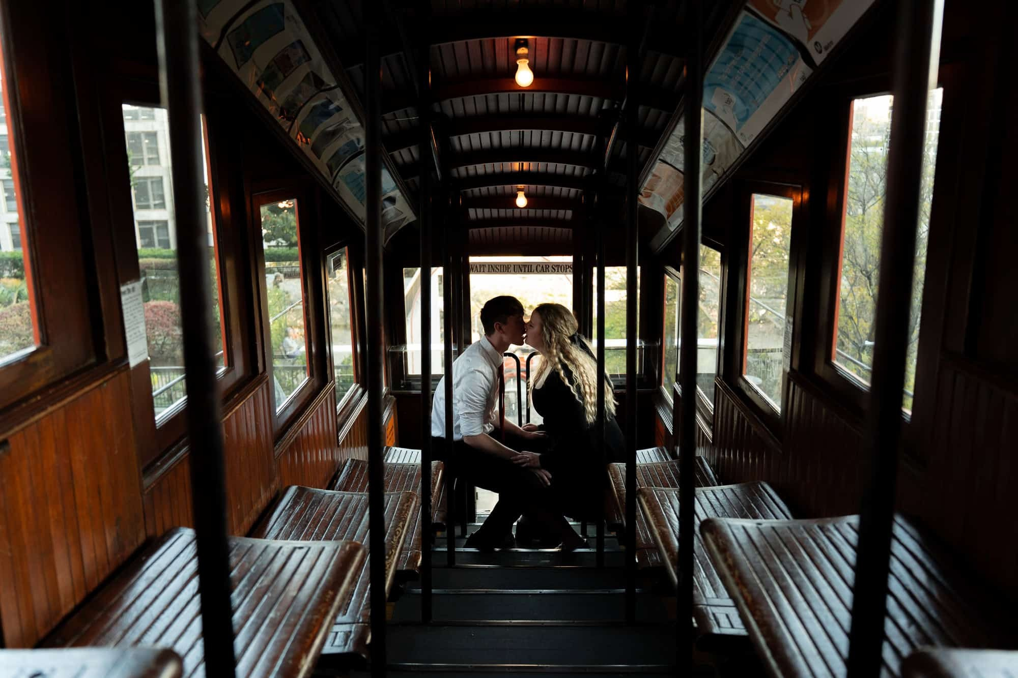 Engaged couple sitting inside the vintage orange Angels Flight Railway car in Downtown LA, sharing a quiet, romantic moment with city textures around them