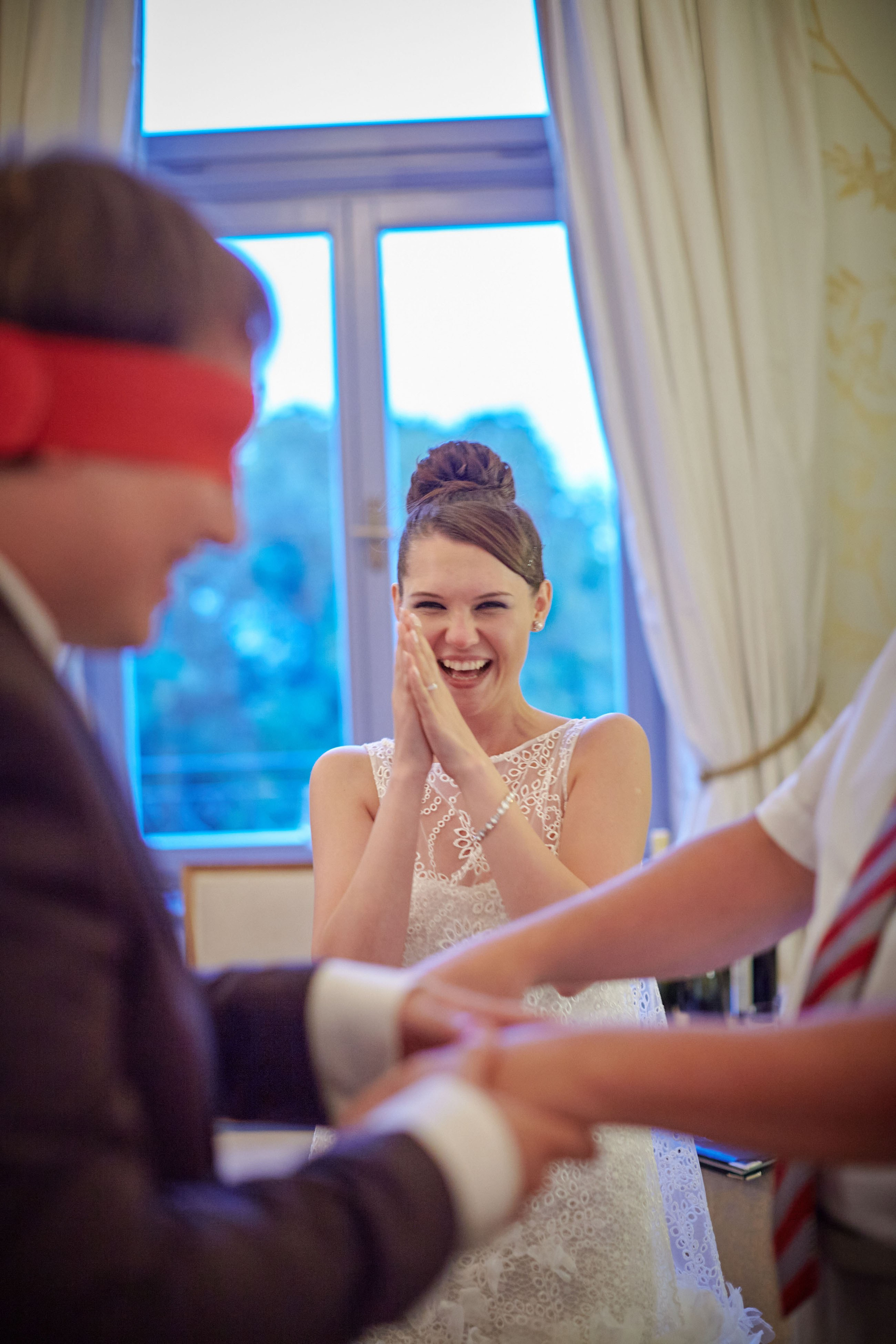 A blindfolded groom amusingly fumbles to locate his laughing bride, relying solely on touch in a playful wedding game.