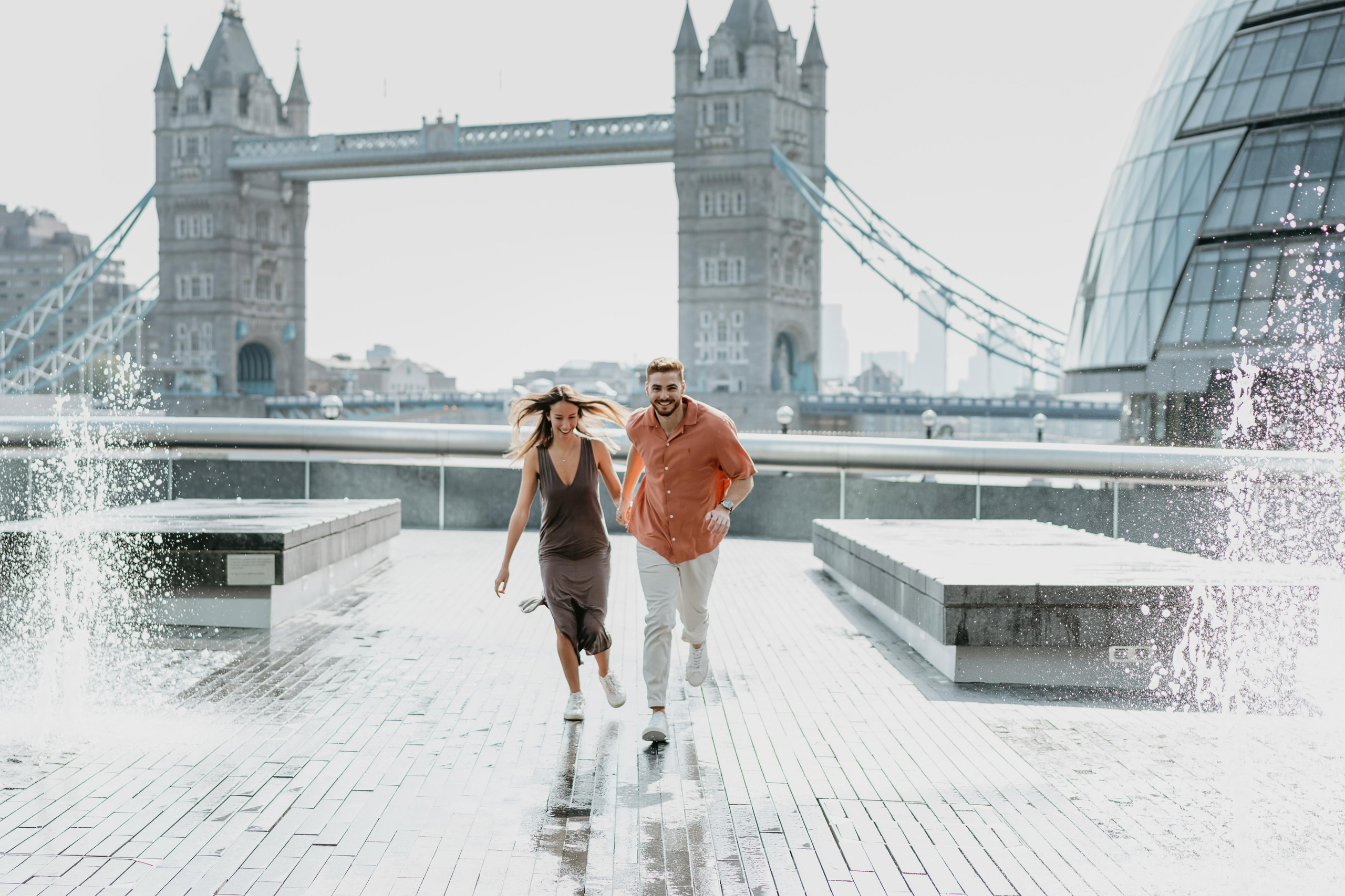 young couple holding hands together and running with tower bridge on the background
