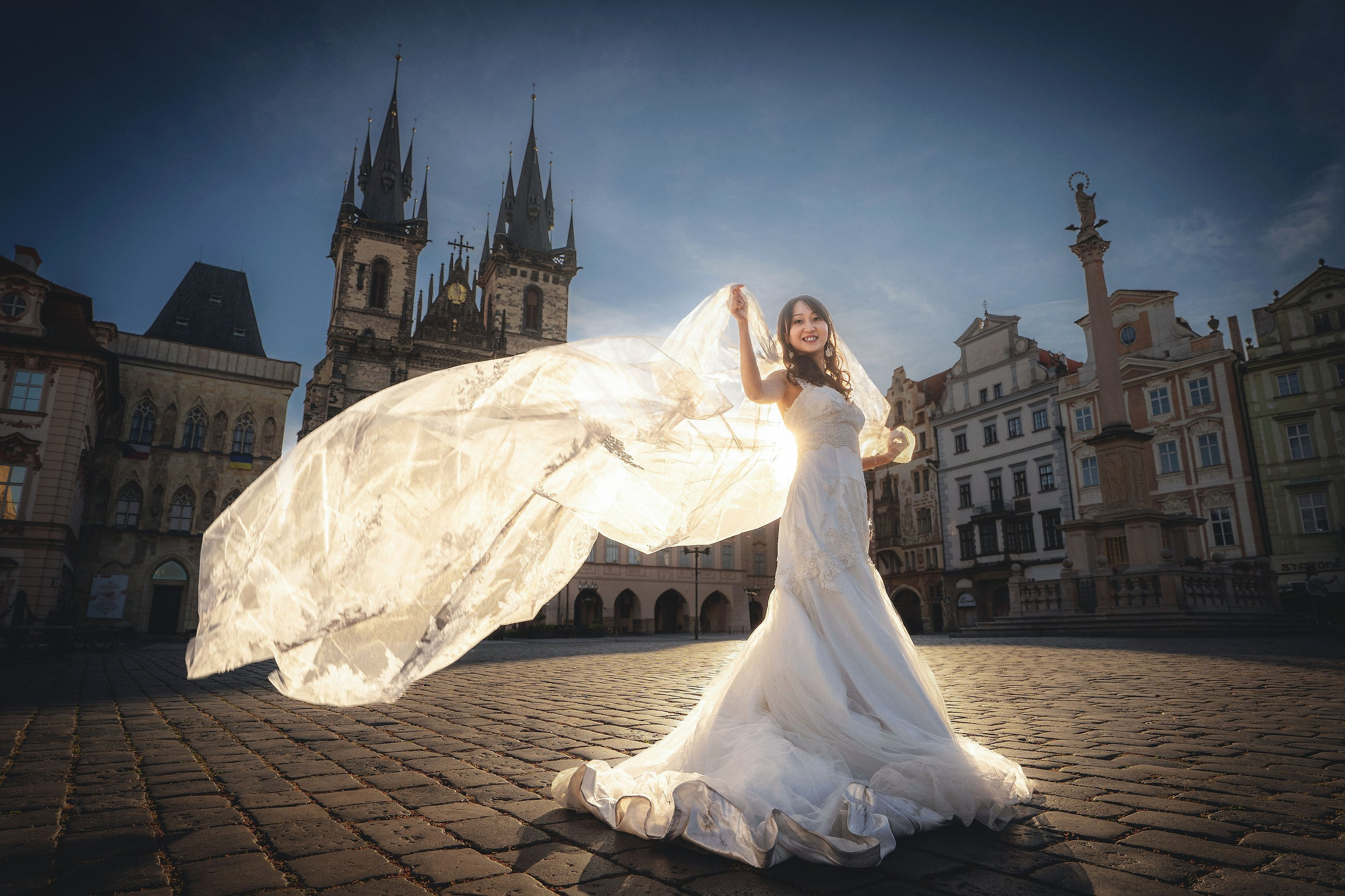 Bride Eva with flowing veil, dramatically backlit by sunrise in Old Town Square, Prague.