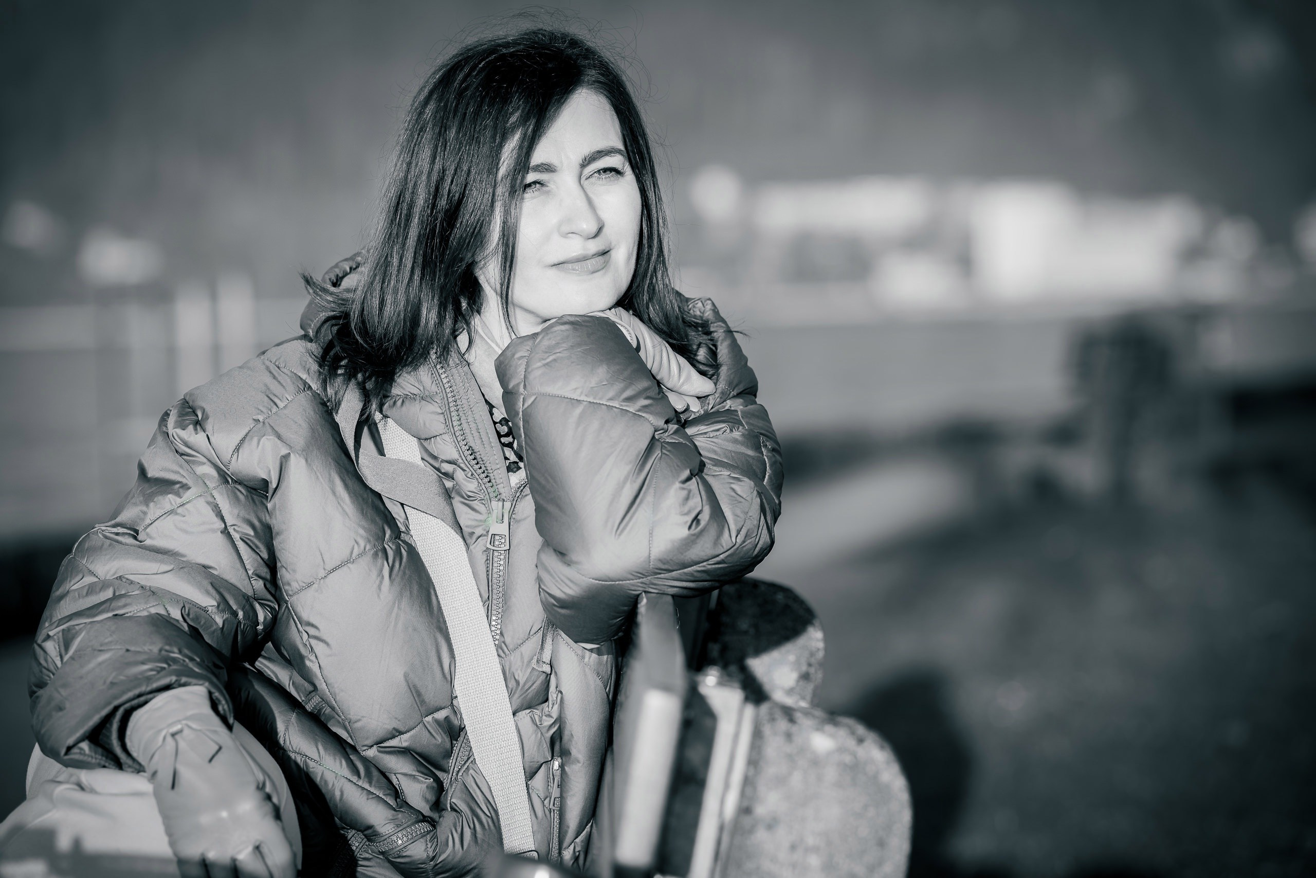 Ein Porträt einer jungen Frau in einer Daunenjacke am See, sitzend auf einer Bank