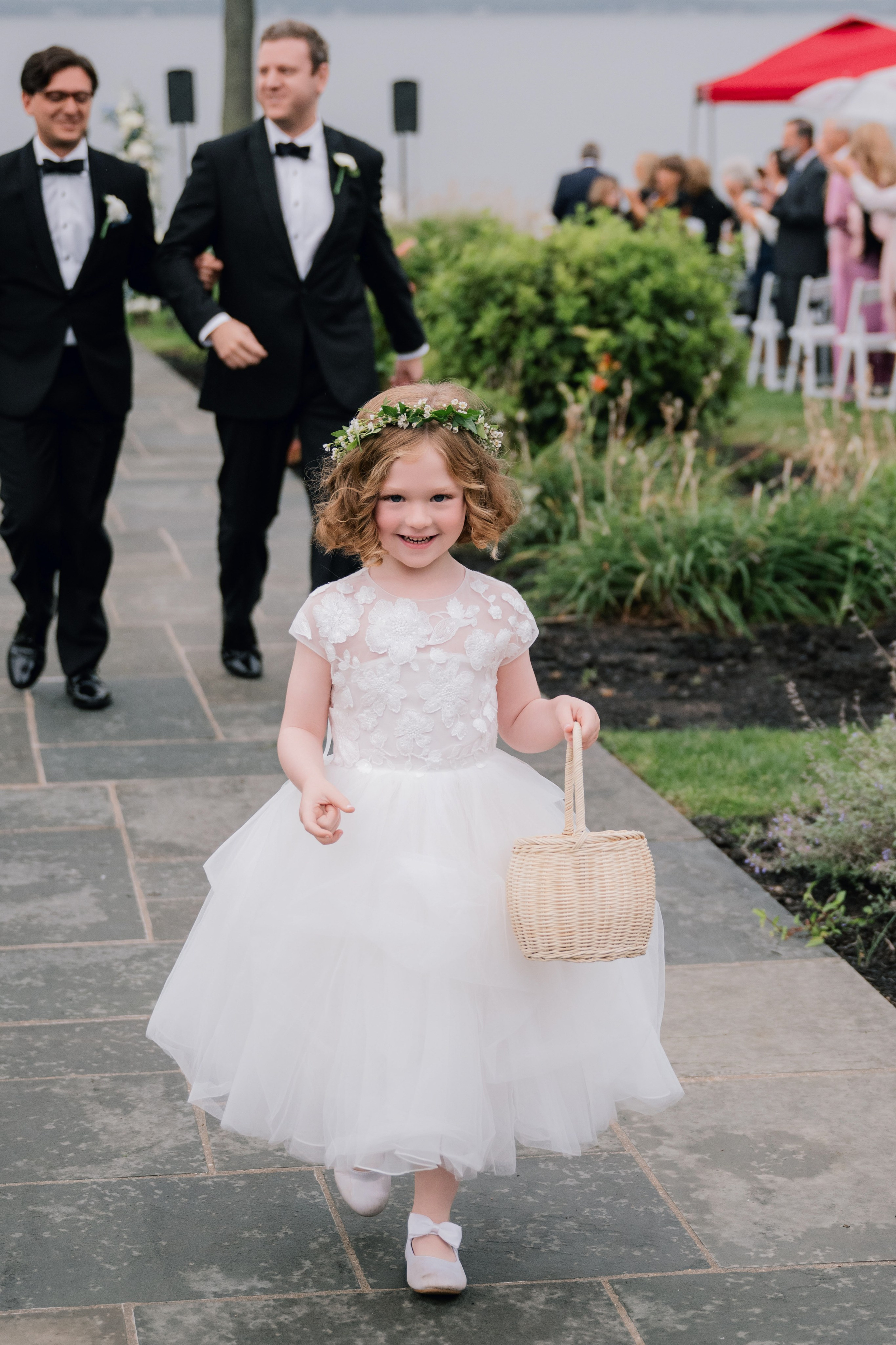 a little girl in a white dress and a flower crown walks down the aisle