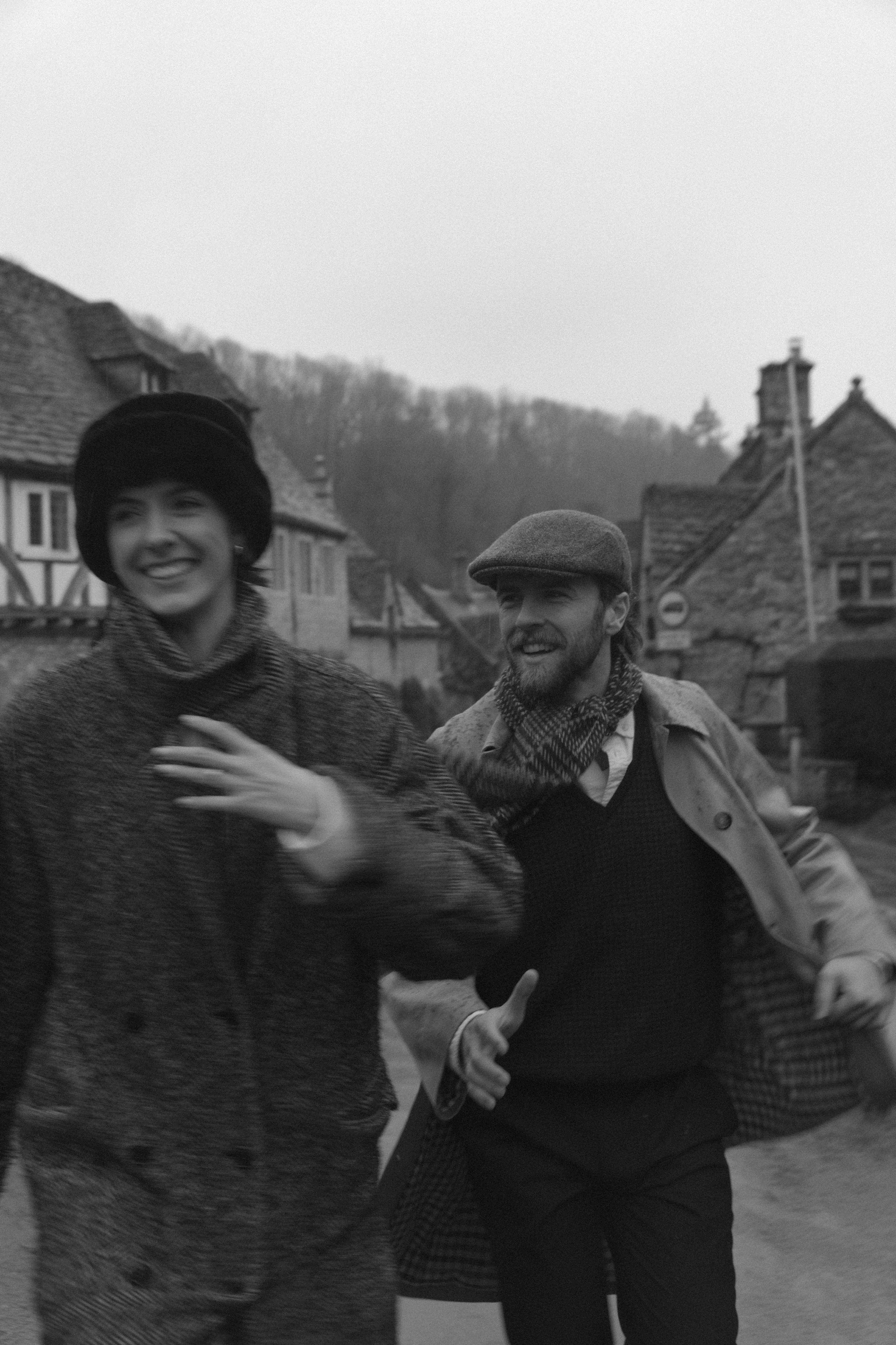 couple running in rain through Cotswolds village with motion blur cinematic engagement photoshoot