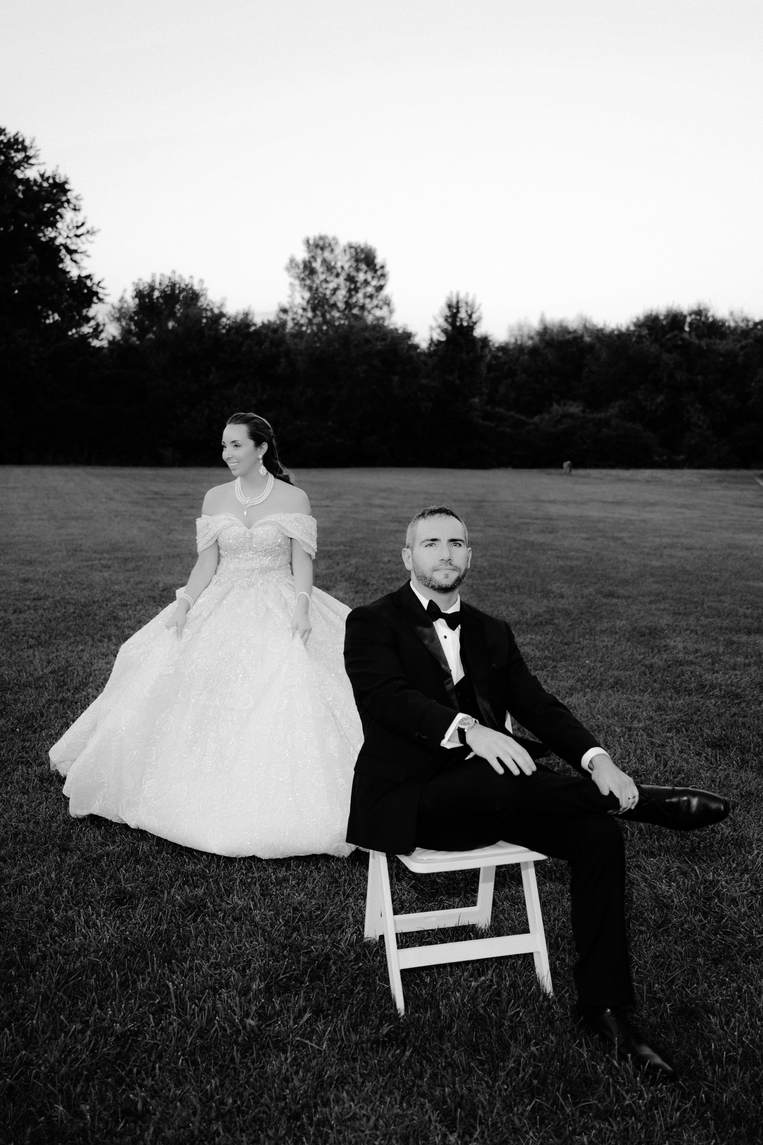 a bride and groom sitting on a chair in the grass