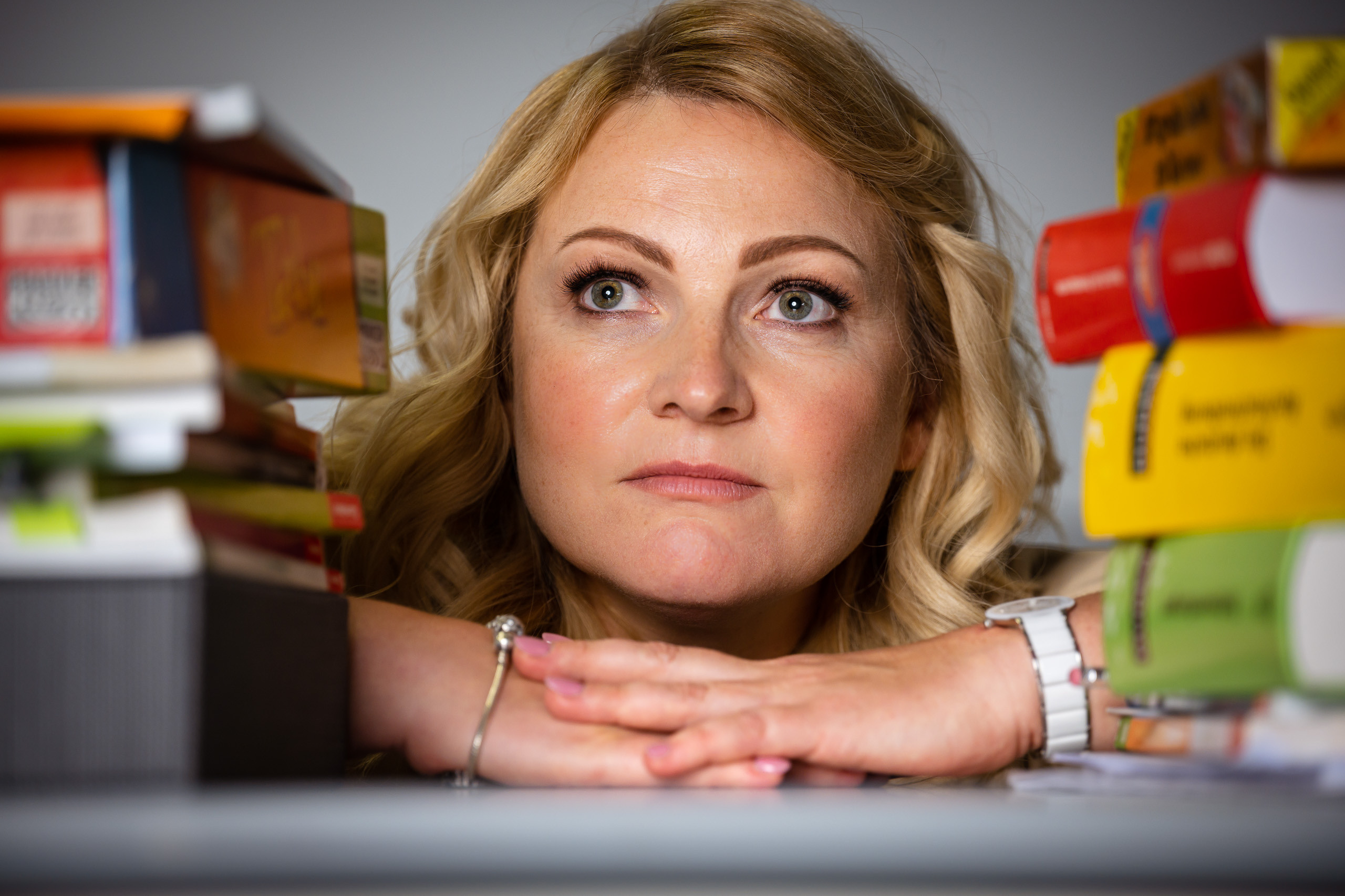 Eine erfahrene, nachdenkliche Lehrerin lugt geheimnisvoll aus einem Stapel Bücher hervor.