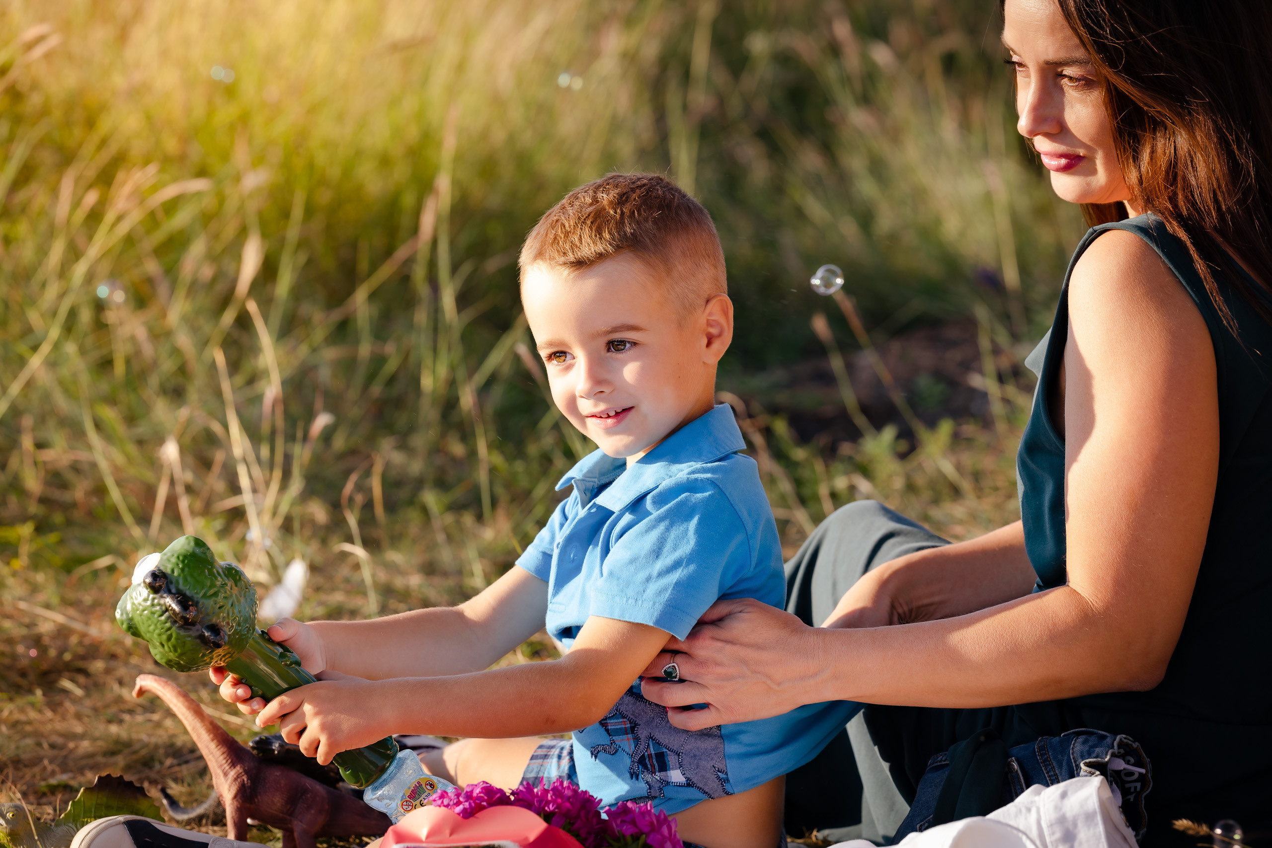 Eine Mutter und ihr Kind sitzen auf einer Wiese mit hohem Gras und spielen mit Seifenblasen.