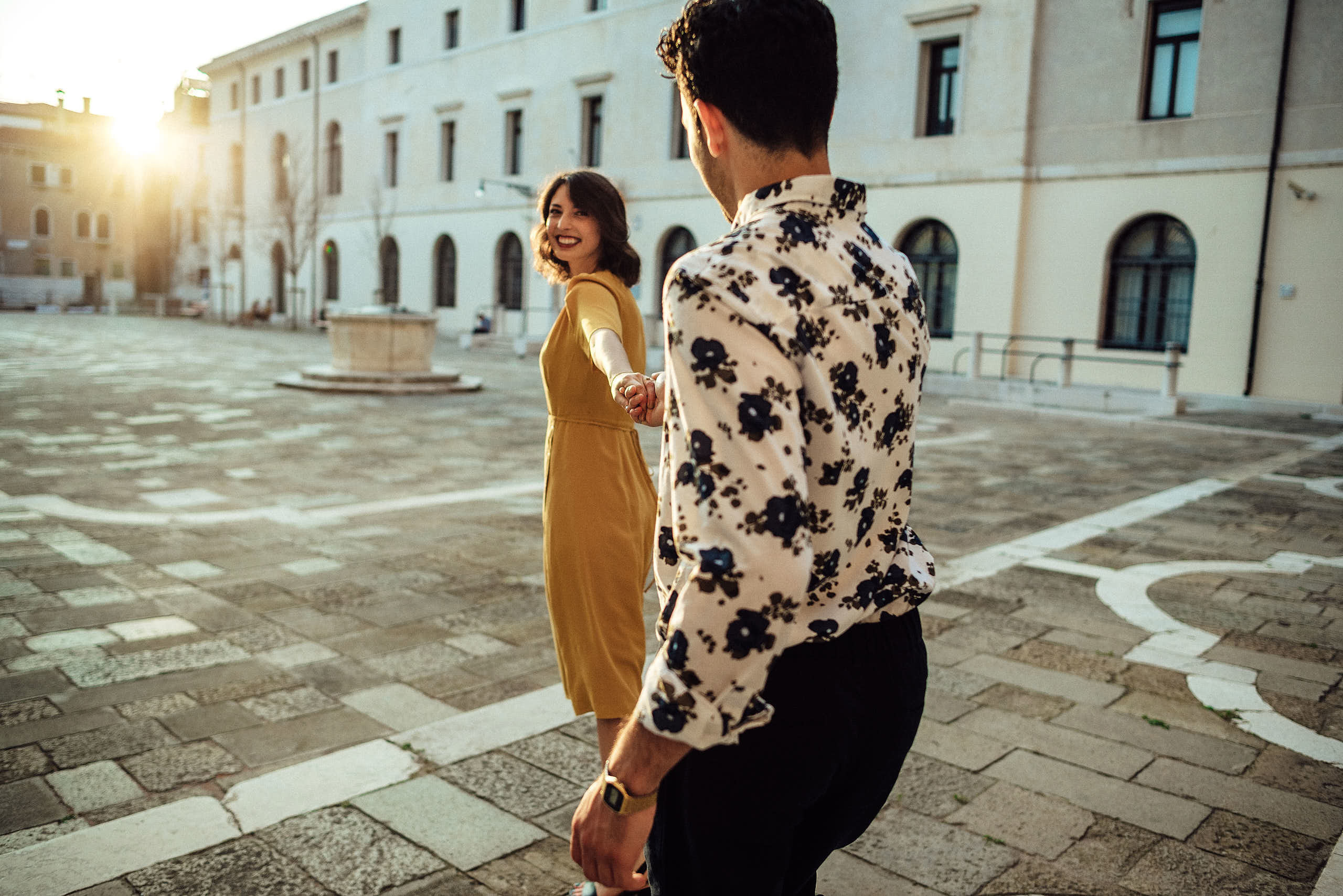 pretty dreesd girl holding hand of her fiance and smiling in street of venice