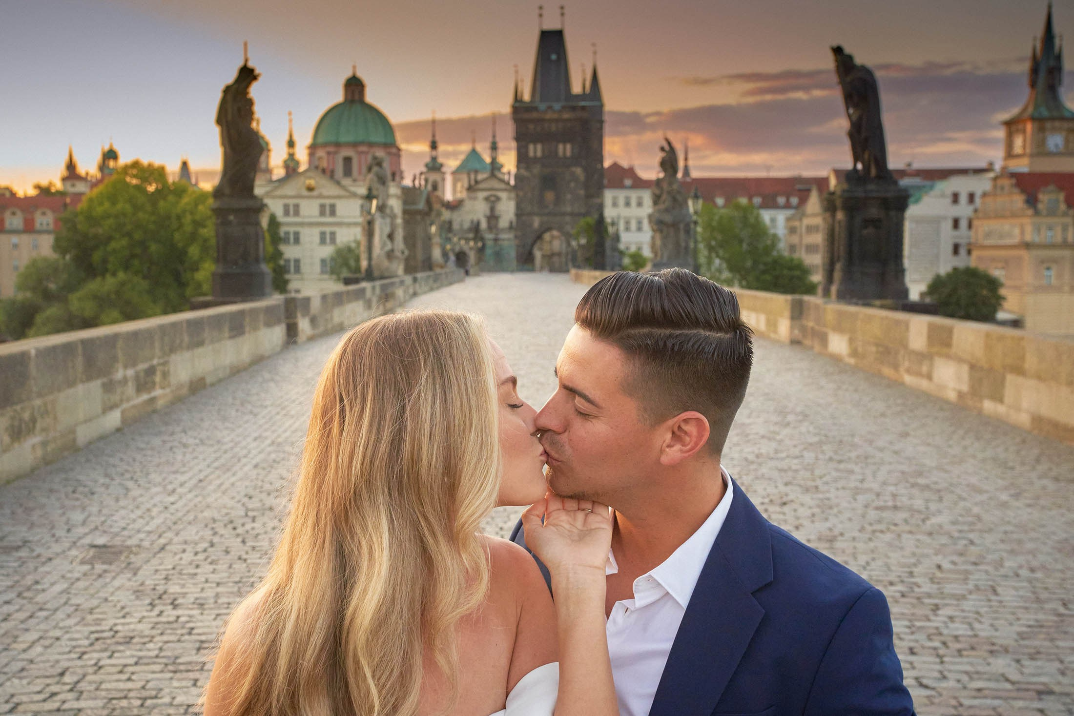 Engaged duo basking in golden hour light on Prague's medieval Charles Bridge.