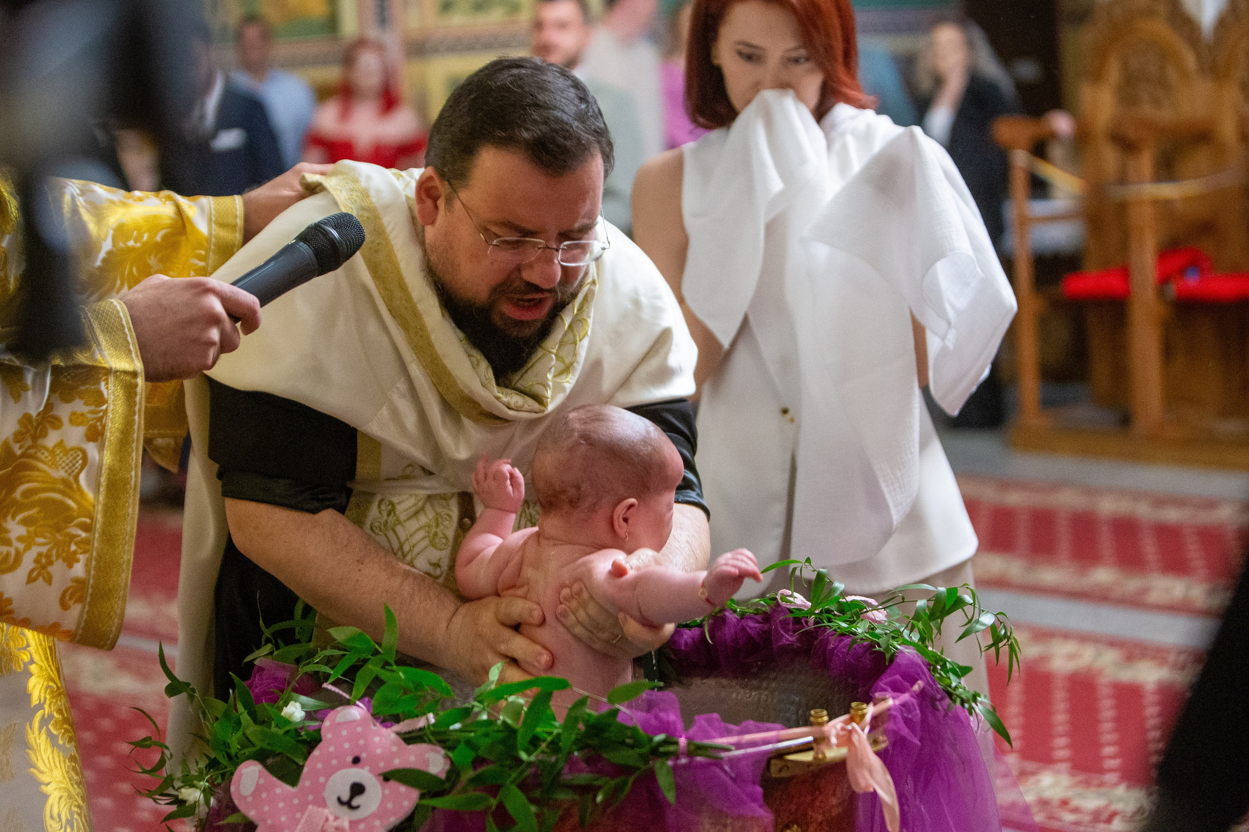 Priest holding baby over baptismal font during church baptism ceremony.