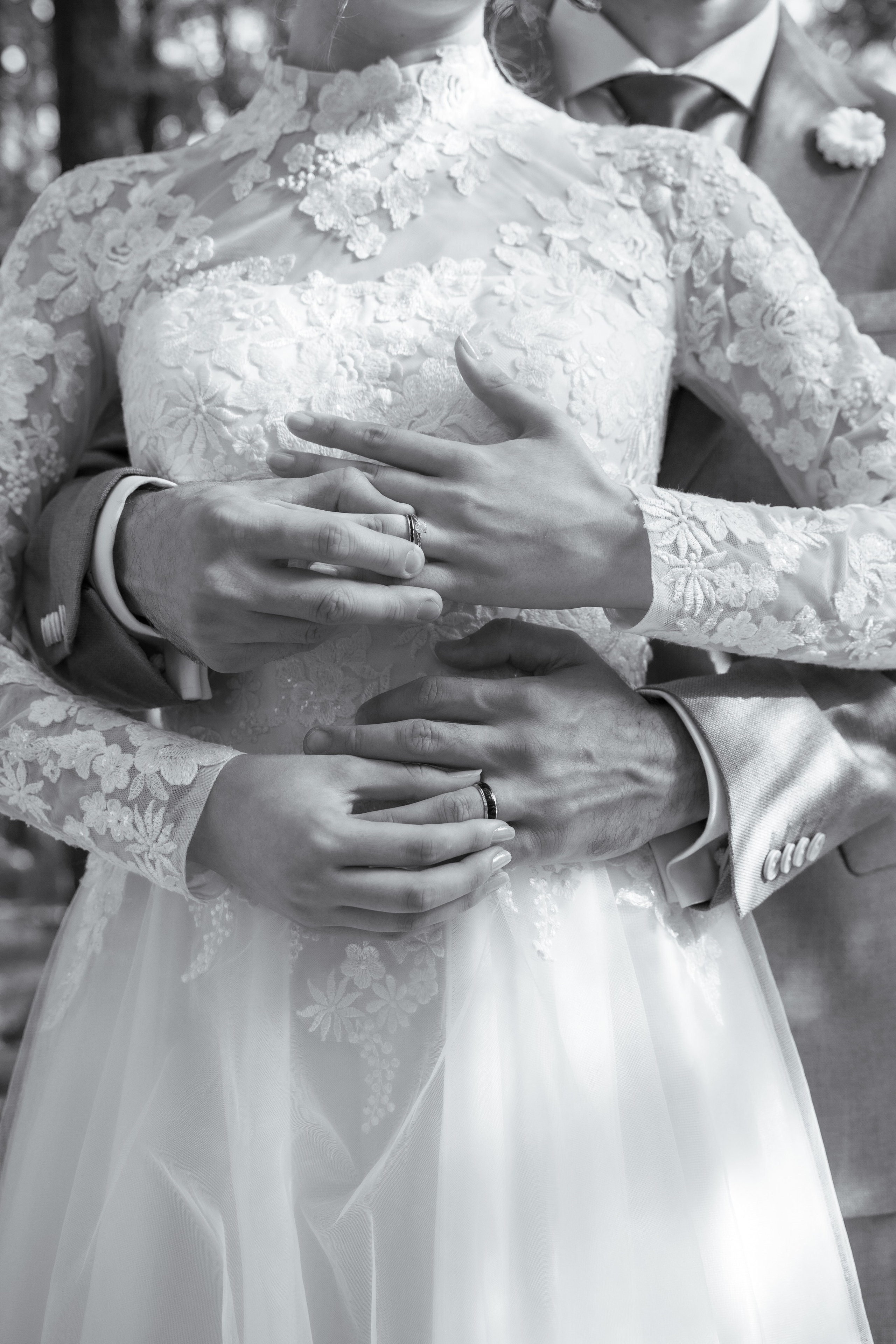 Detaliu alb-negru cu mâinile mirilor și verighete, mireasă în rochie cu dantelă, fotografie artistică de nuntă incadru.ro.
