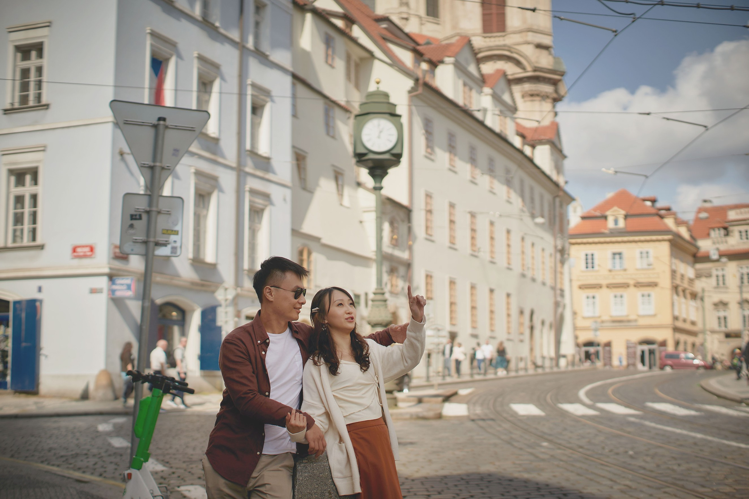 Eva and Conan are exploring the street in Malá Strana with a large clock and tram line.