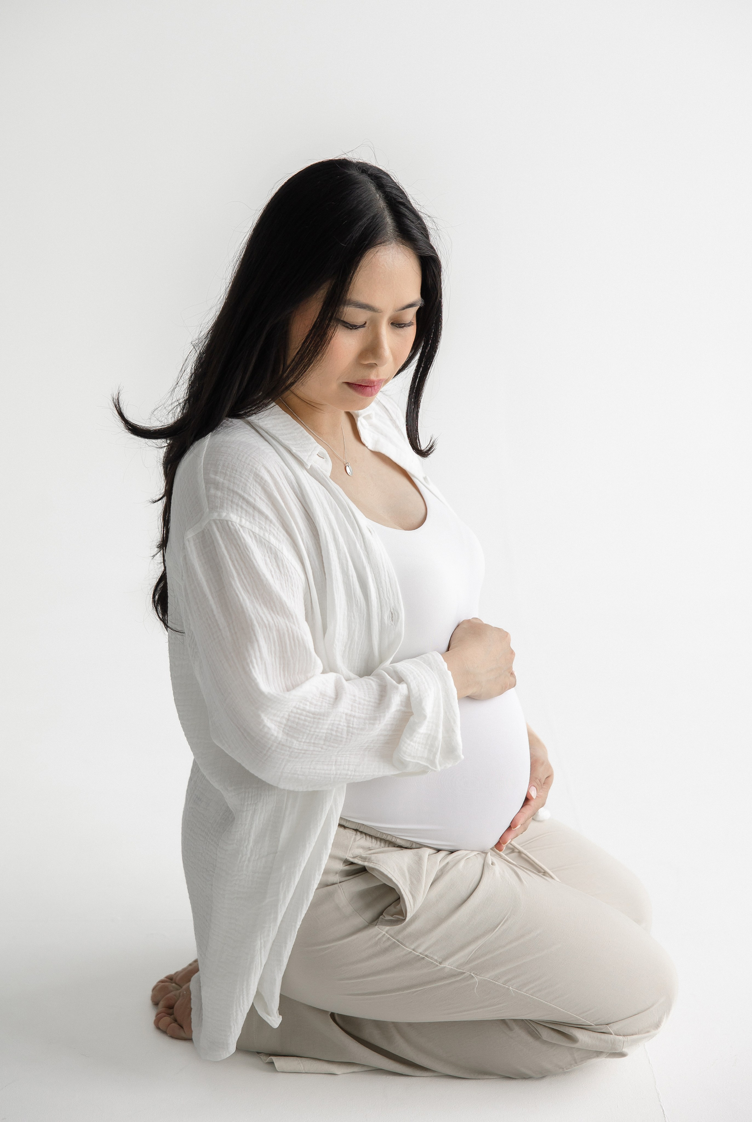 Pregnant woman kneeling and holding baby bump during minimalist maternity photoshoot – calm, elegant pregnancy photography in Toronto by Iana Banana