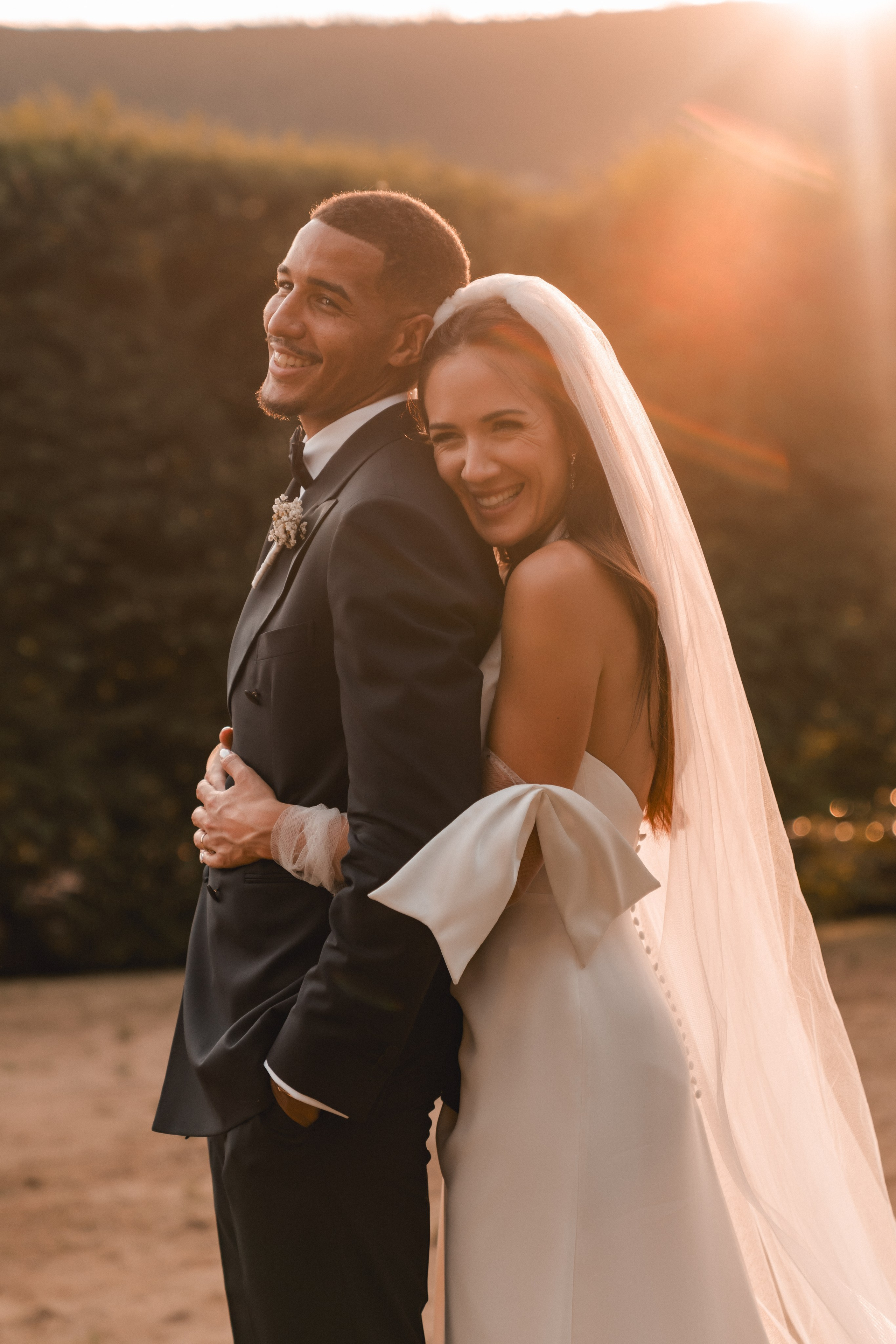 Noivos sorridentes abraçados ao entardecer, rodeados por árvores e luz suave em quinta do norte.