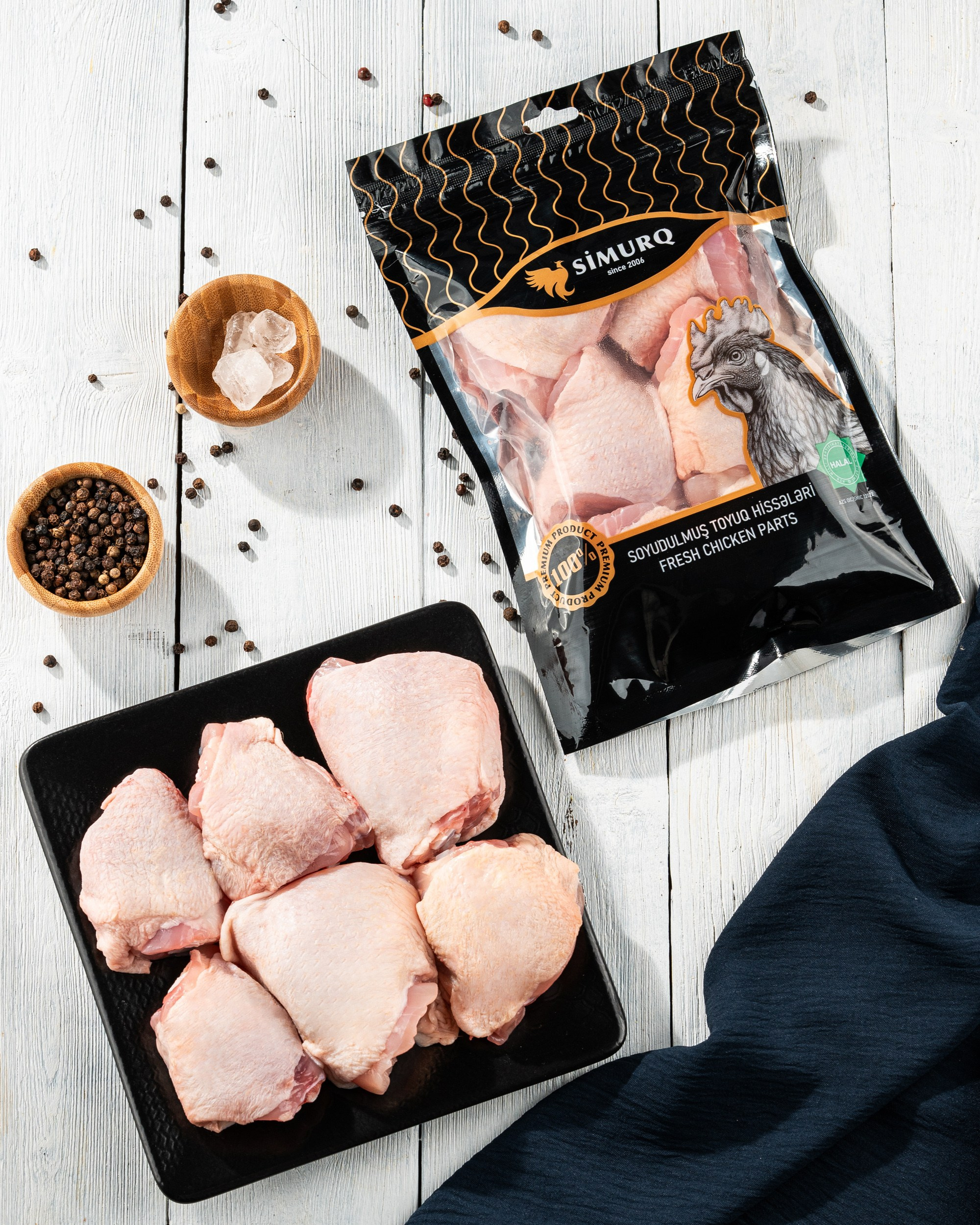 Simurq brendinə aid soyudulmuş toyuq bud hissələri – paketdə və qara boşqabda qara istiot və buz ilə məhsul təqdimatı