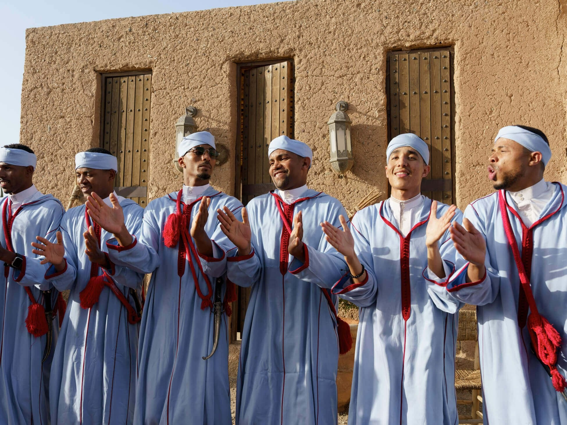 Musicians clapping beside textured wall at destination desert wedding, Morocco