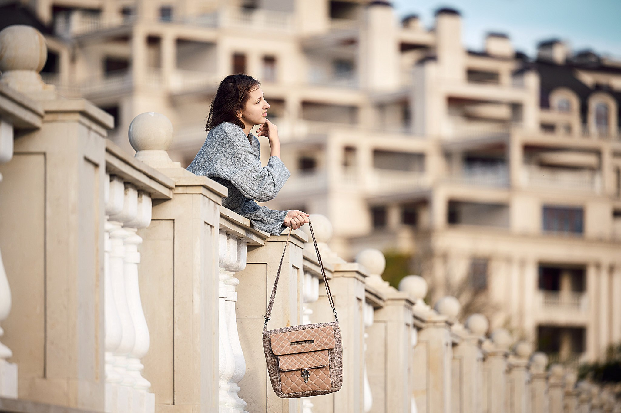 Портрет девушки в сером вязанном костюме и бежевой сумкой с распущенными каштановыми волосами