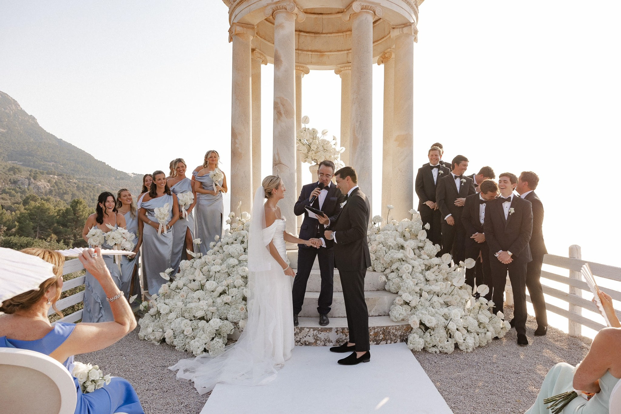 Bride and groom holding hands with their wedding officiant at the Son Marroig temple, surrounded by bridesmaids and groomsmen