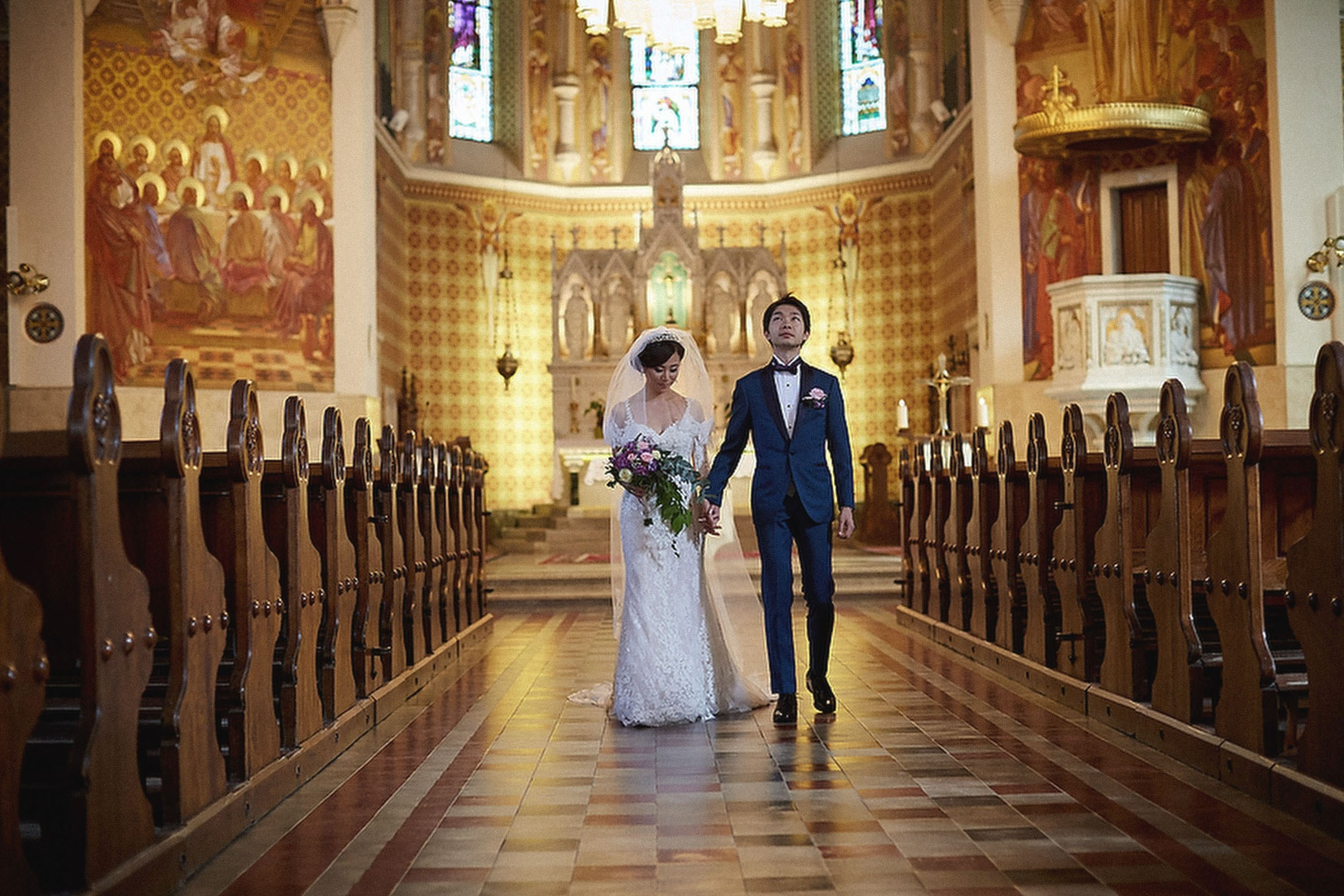 A bride and groom walk hand in hand down the aisle as they exit a church following their wedding ceremony.