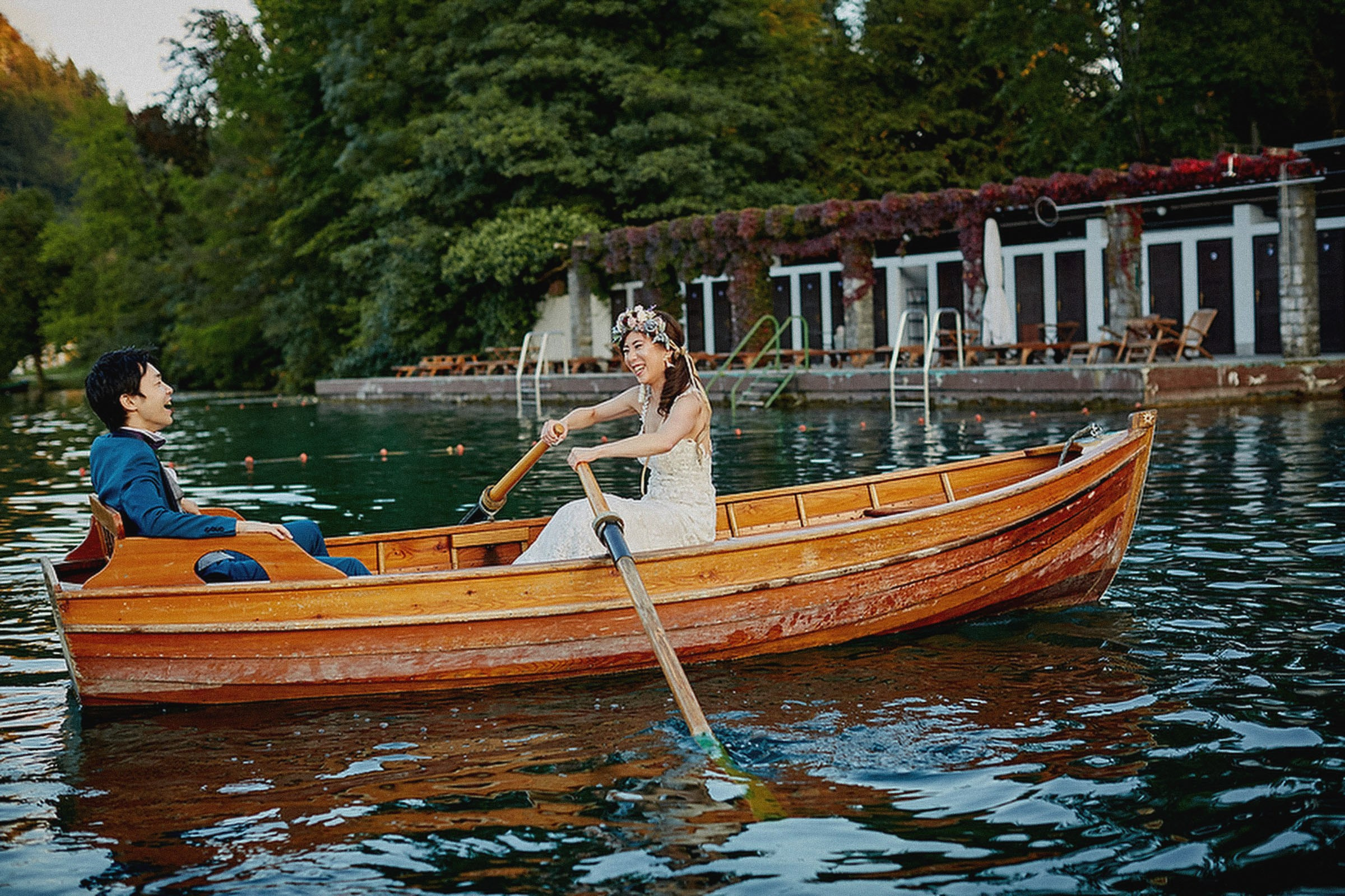 A smiling, yet tired Japanese bride rows the boat into the dock as her groom enjoys the ride.