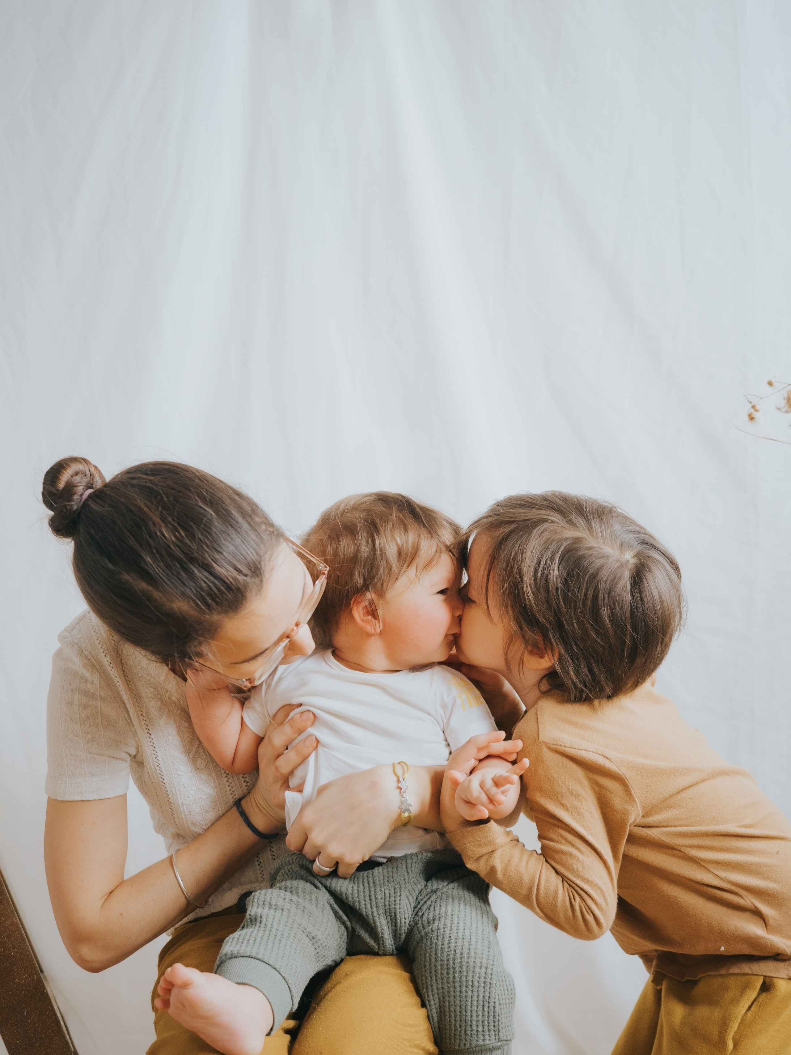 Mother and brother kissing younger sibling.