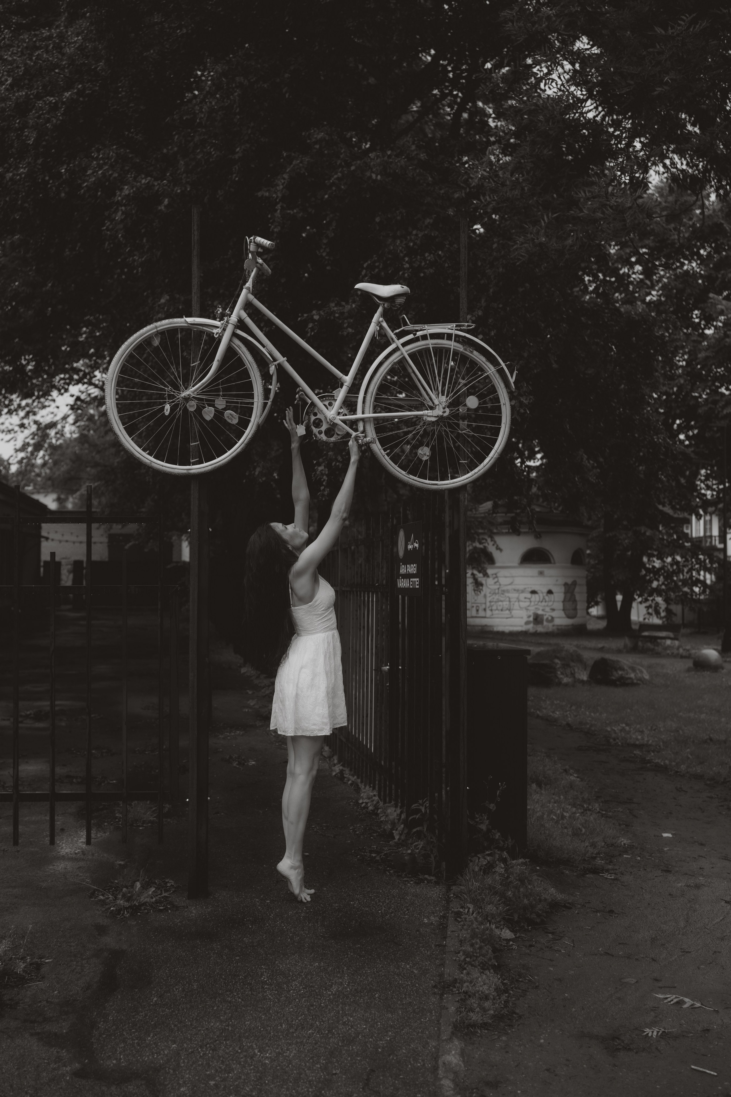 Fine art portrait of a woman standing under a bicycle, urban outdoor scene, Tallinn