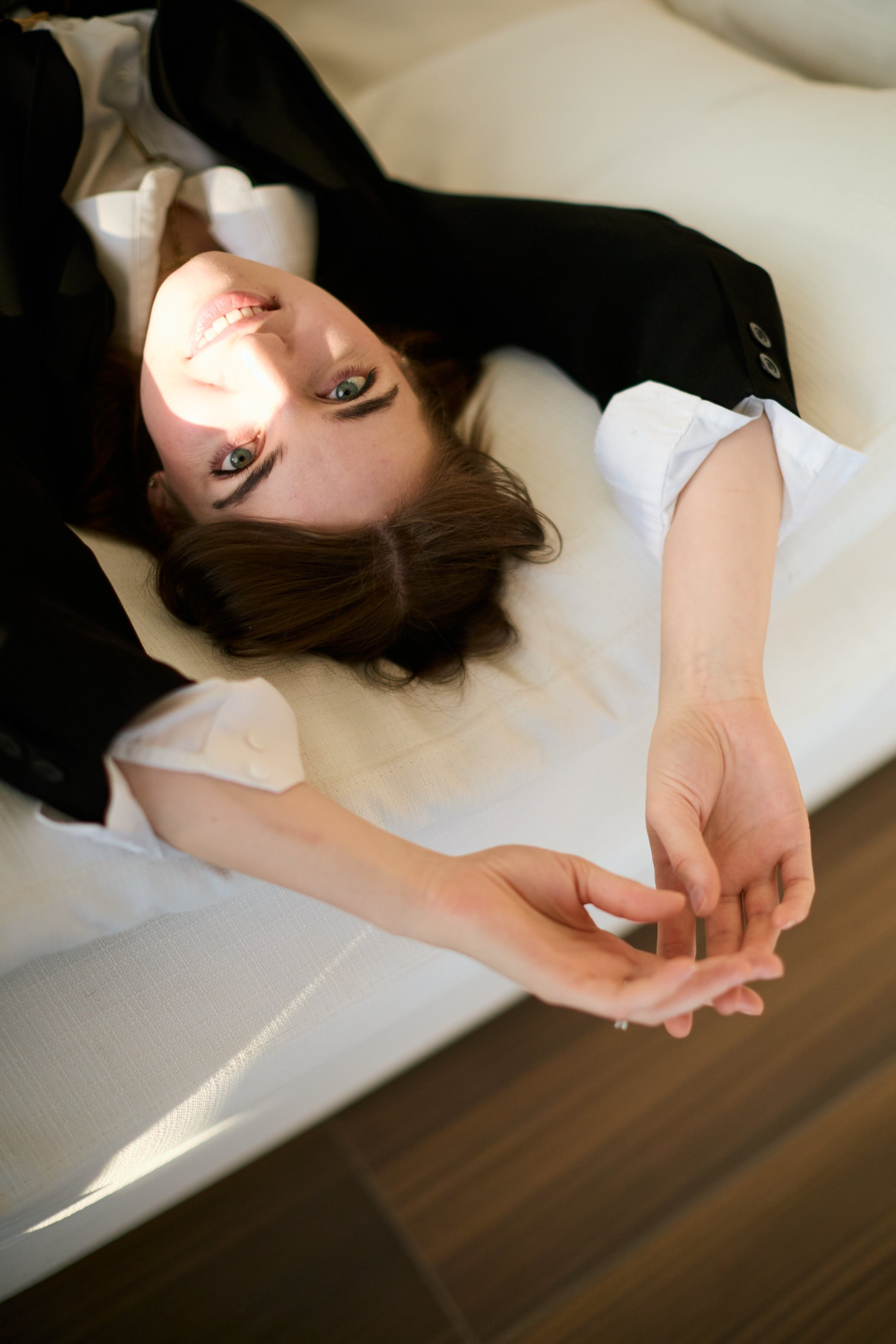 Woman in a black jacket and white top lying back on a white sofa, looking up at the camera — portrait in Coquitlam