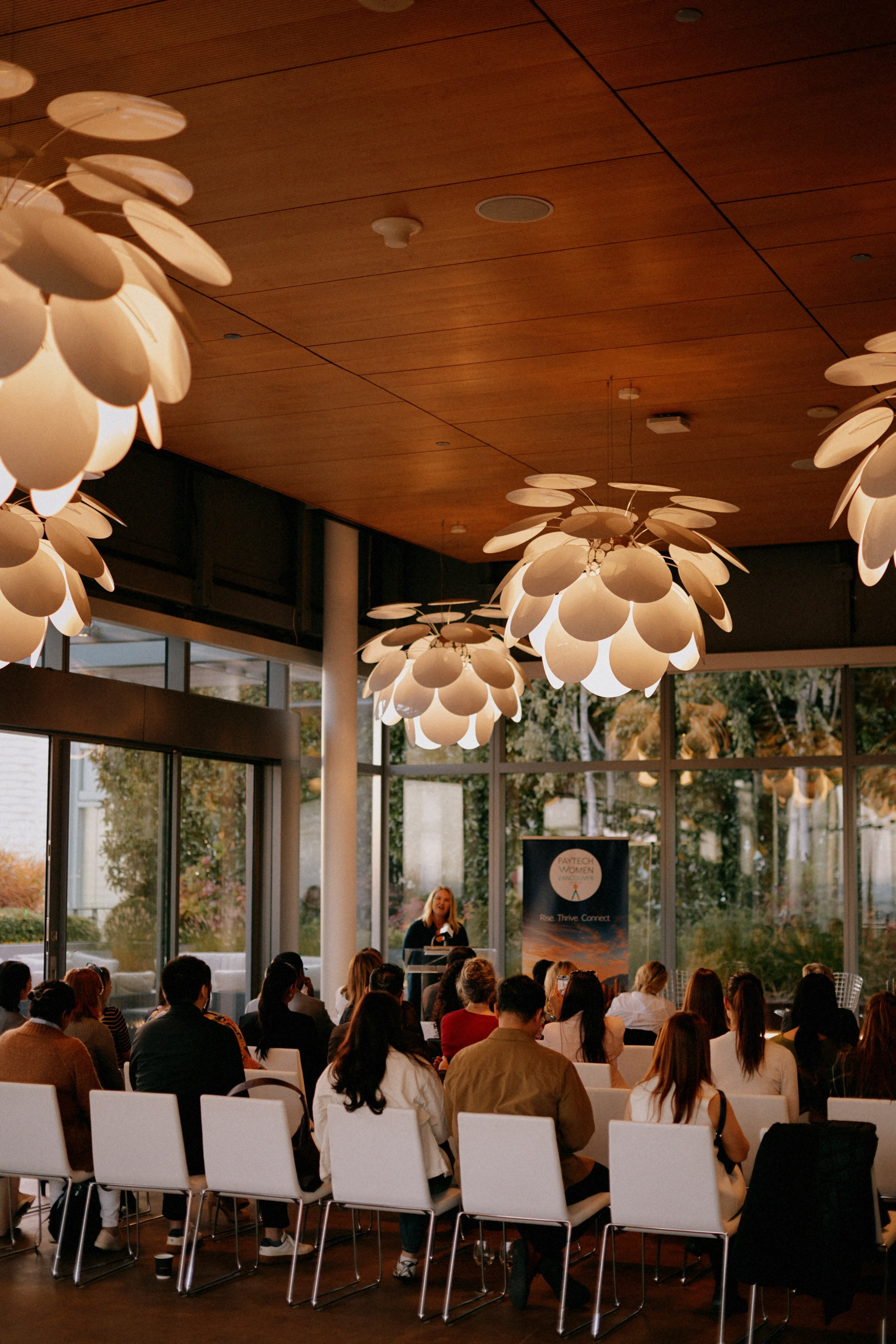 Speaker at the lectern and guests in white chairs at the PayTech Women Vancouver chapter launch, TELUS Garden