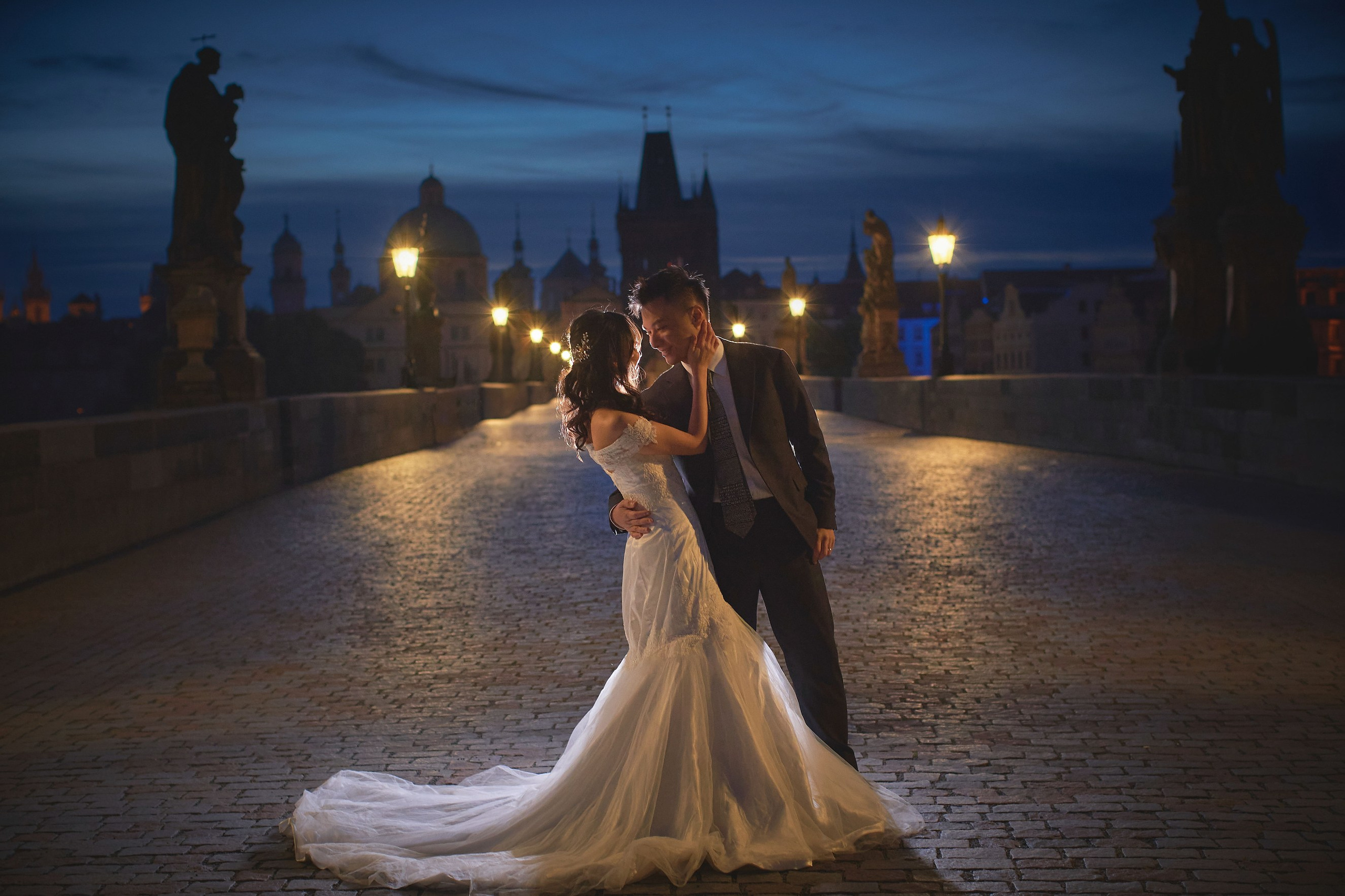 Groom Conan dipping bride Eva in joyful embrace on Charles Bridge at sunrise, Prague.