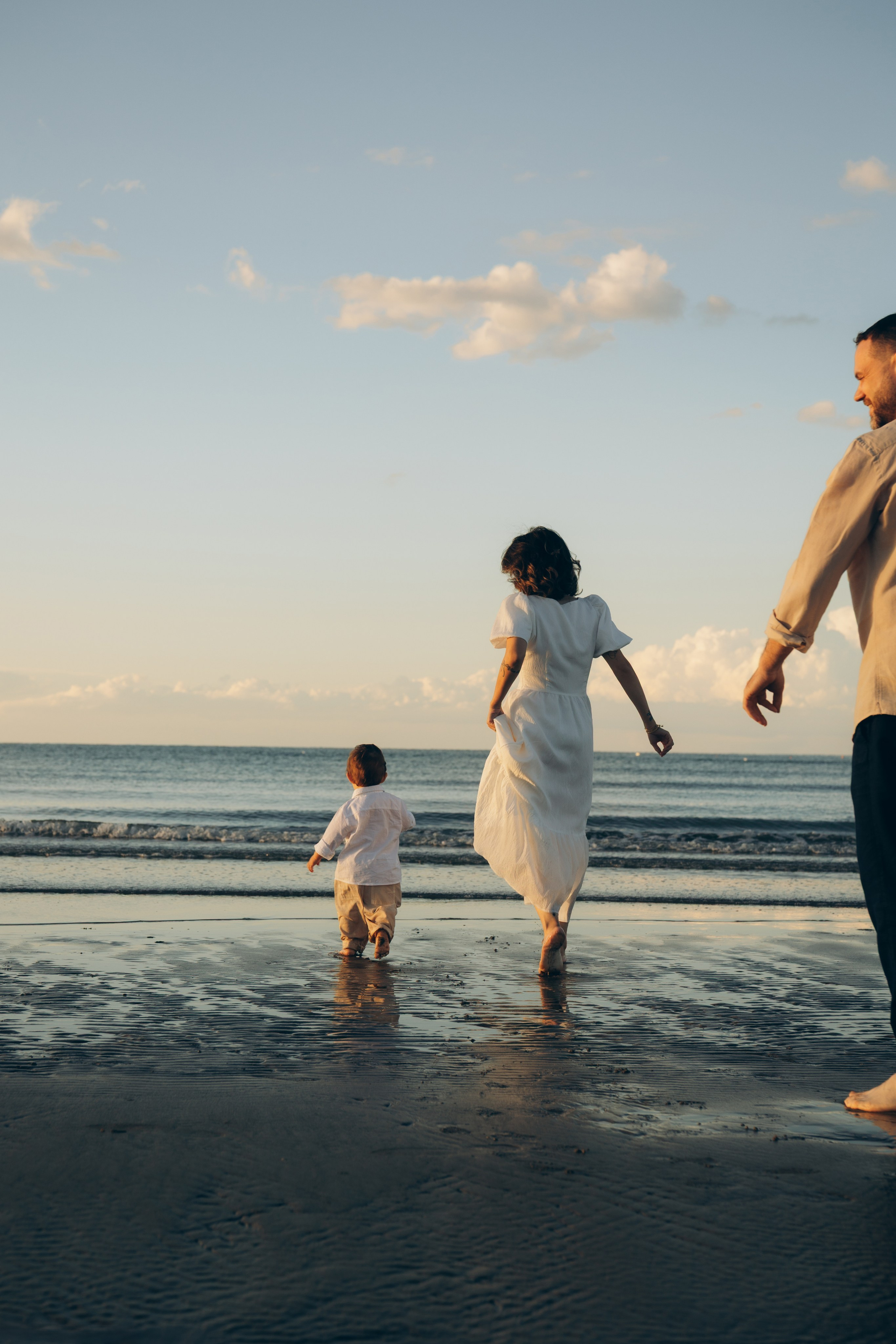 Famiglia con bambino che entra in acqua durante un servizio fotografico a Cesenatico. Gesti spontanei, riflessi sulla sabbia bagnata e atmosfera estiva.