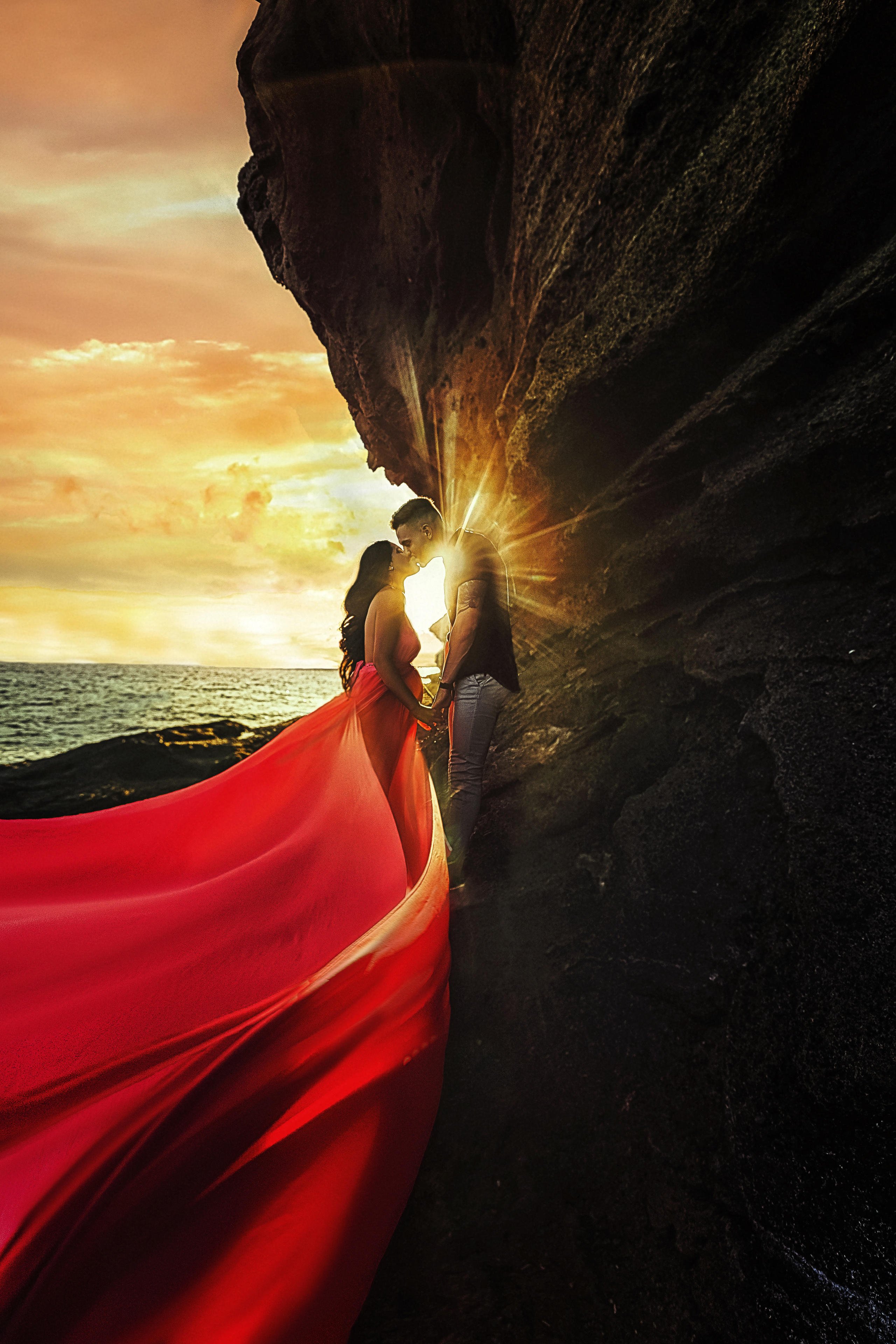 Беременная девушка в шлейфом платье целуется с мужем в лучах заката