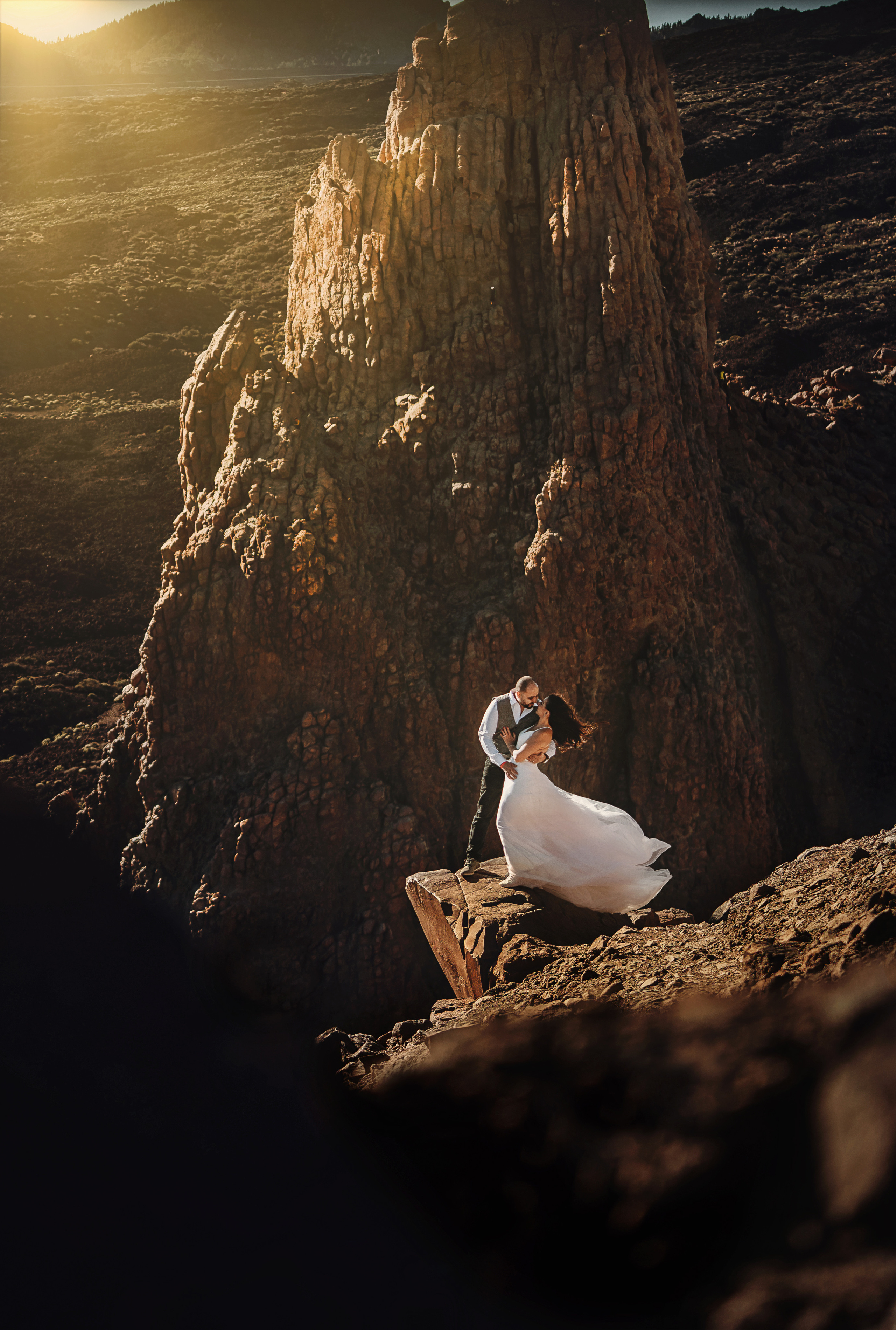 Пара молодожёнов стоят на краю скалы и обнимаются