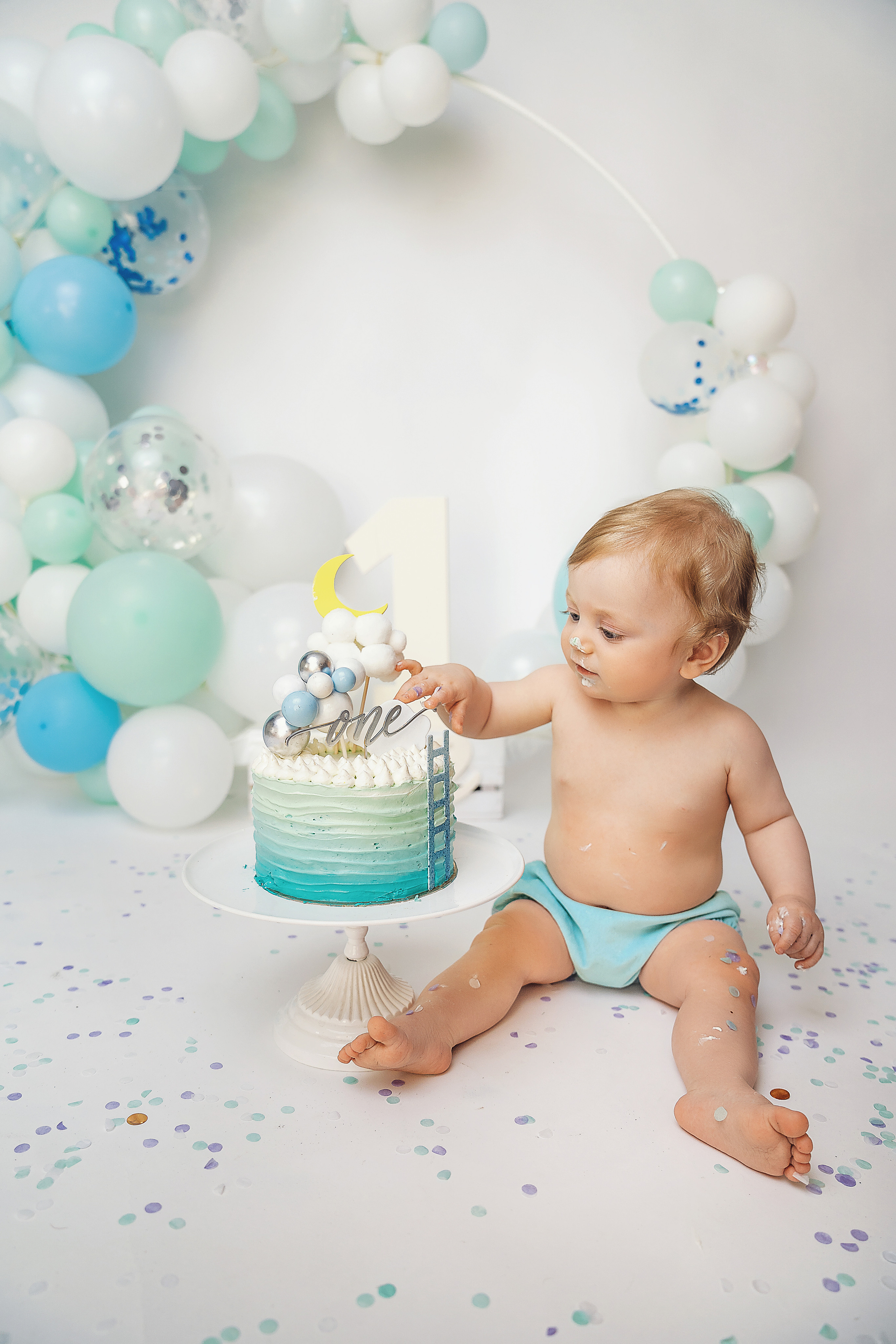 Малыш сидит рядом с тортиком на фоне шариков