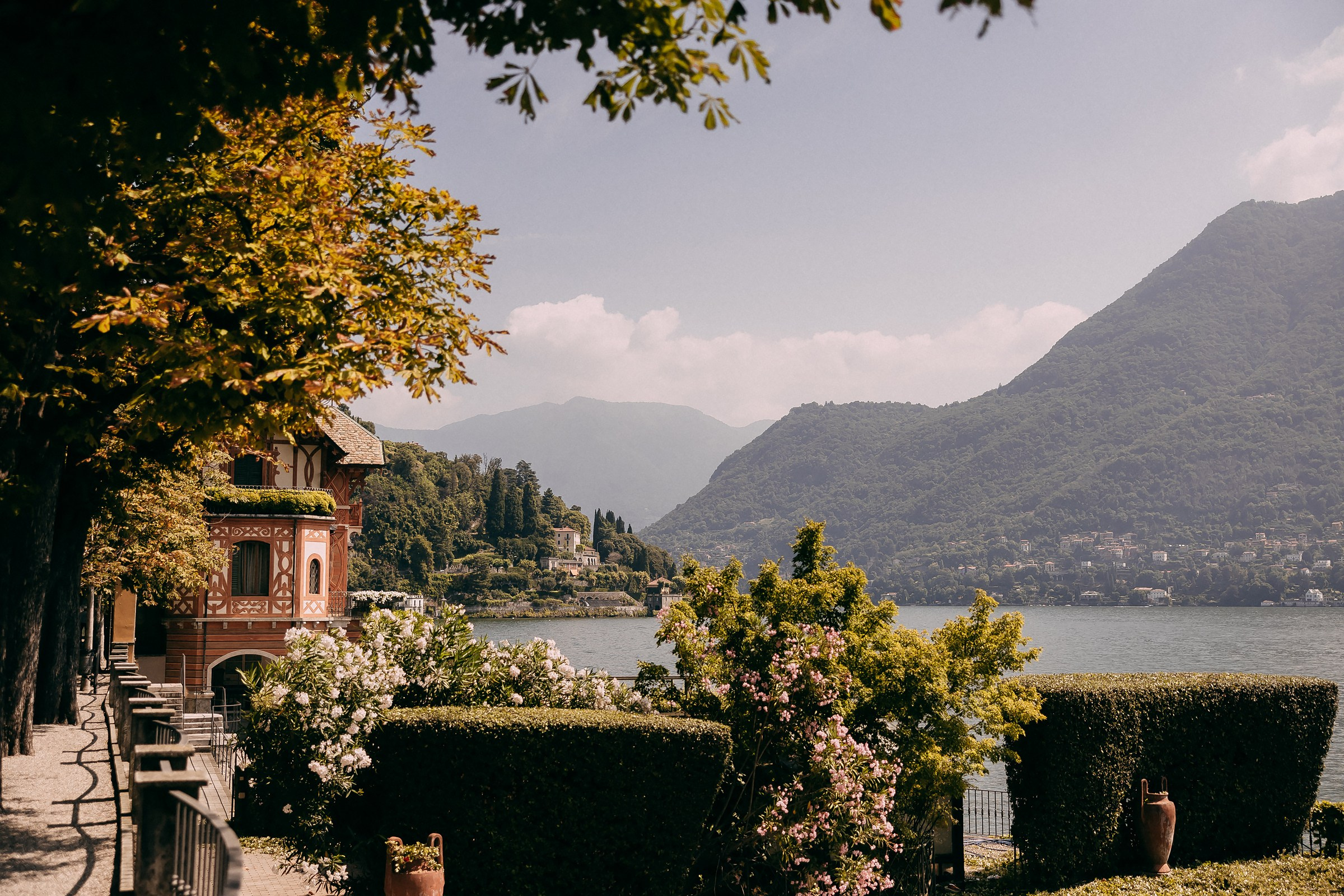 Scenic view of Lake Como with mountains, greenery, and a lakeside villa under clear skies.