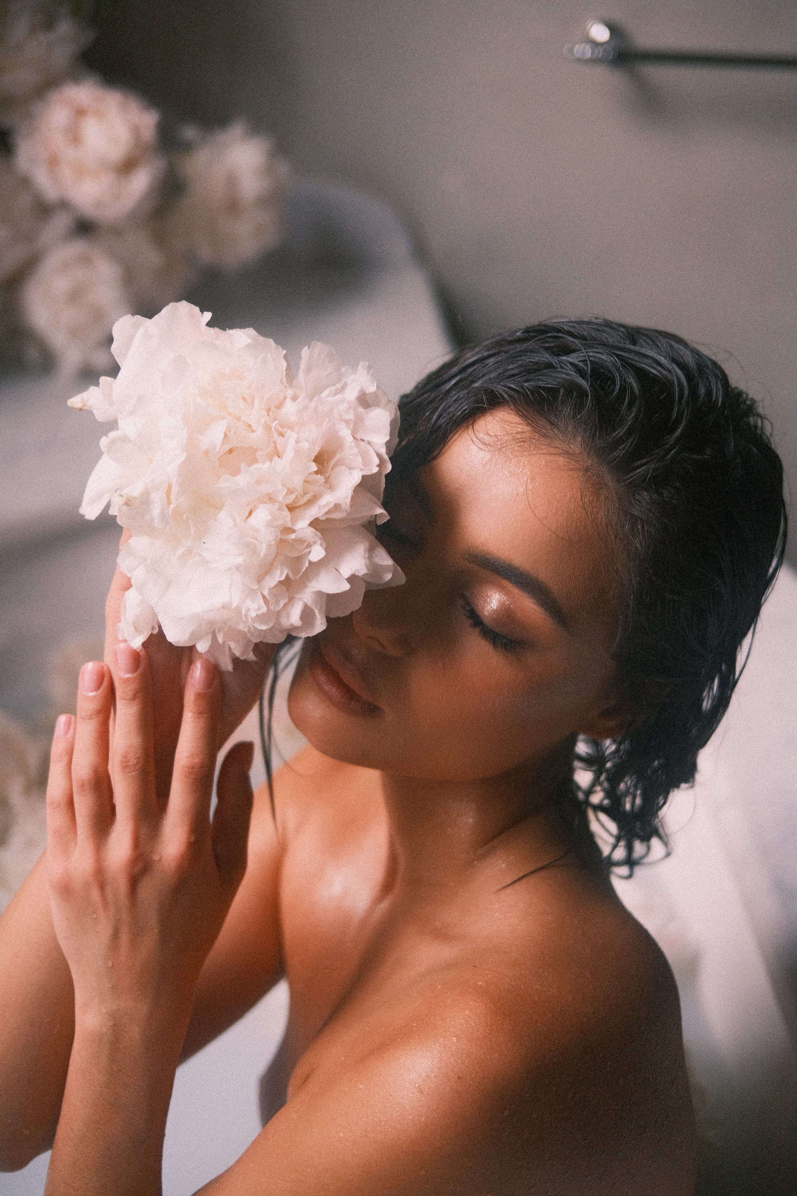 A bride delicately holding a white peony to her face, her eyes closed in a moment of relaxation and sensuality.