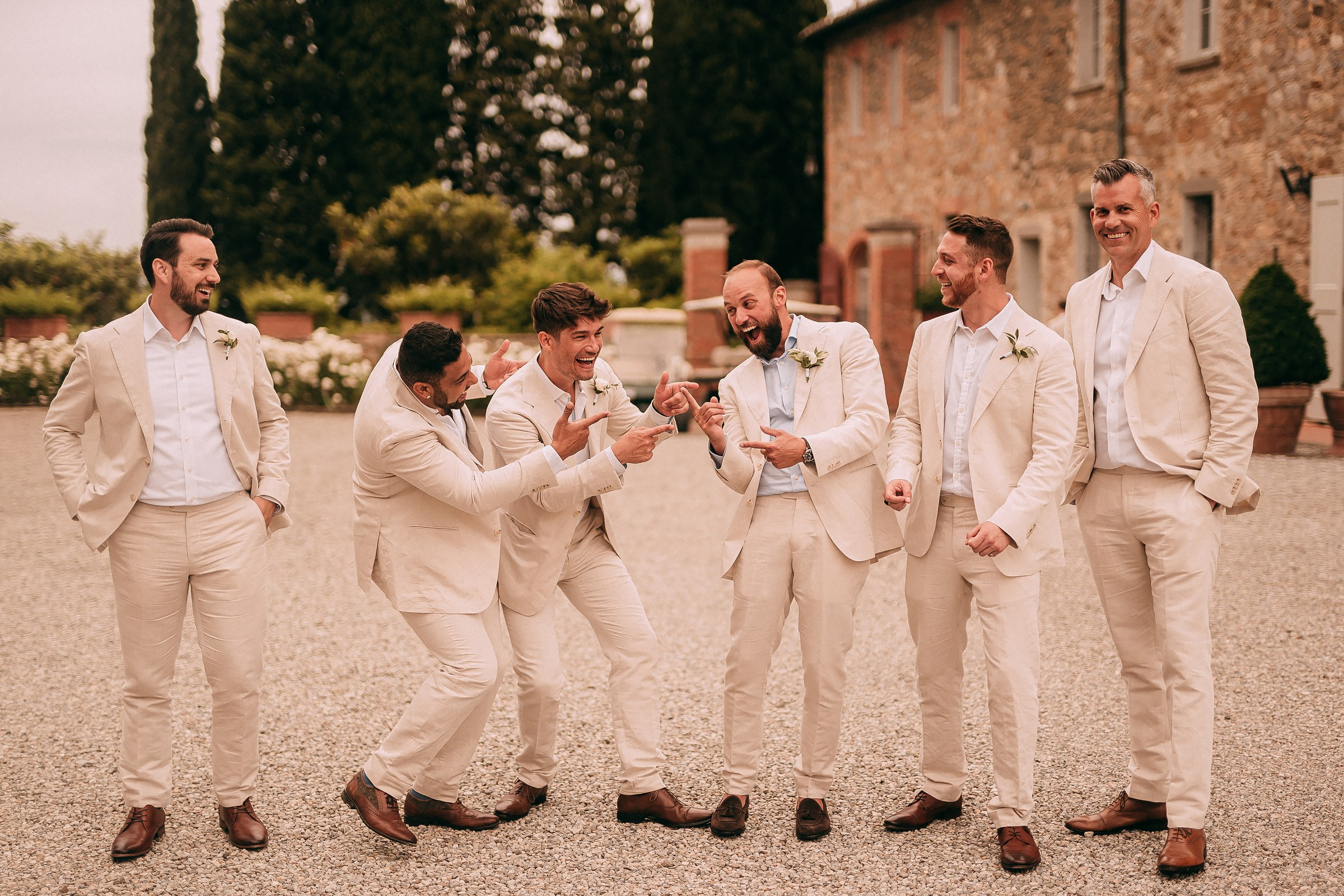 Groomsmen laughing and pointing at each other in a candid moment of joy during wedding festivities.
