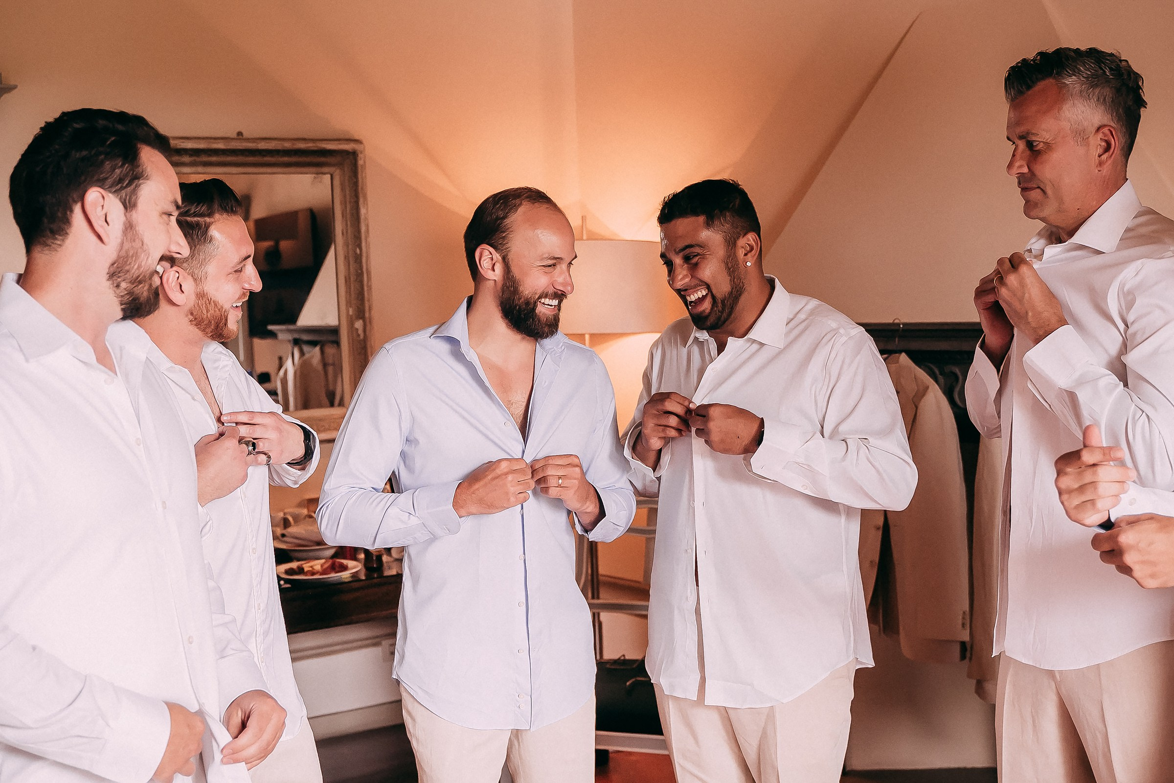 Groomsmen laughing and getting ready in crisp white shirts at Tuscany villa.