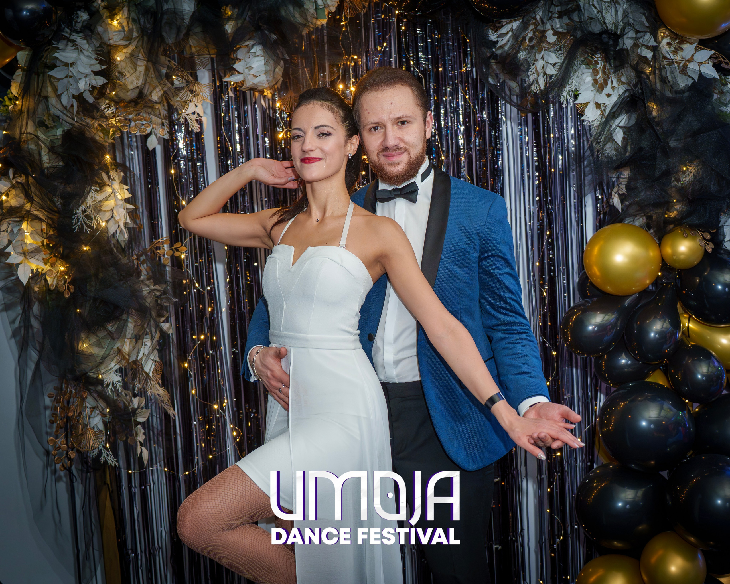 Man and woman posing at Umoja Dance Festival with festive decorations and balloons in background.