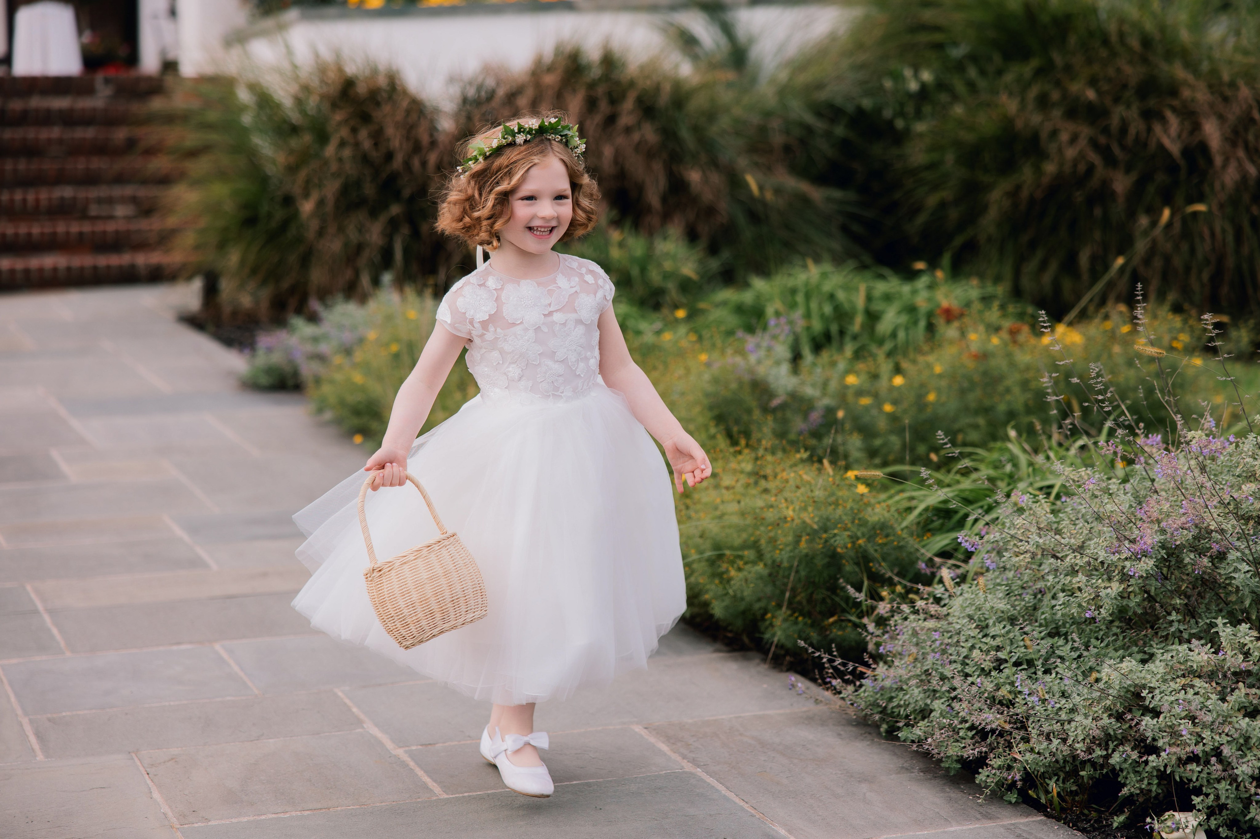 a little girl in a white dress and flower crown walking down a path