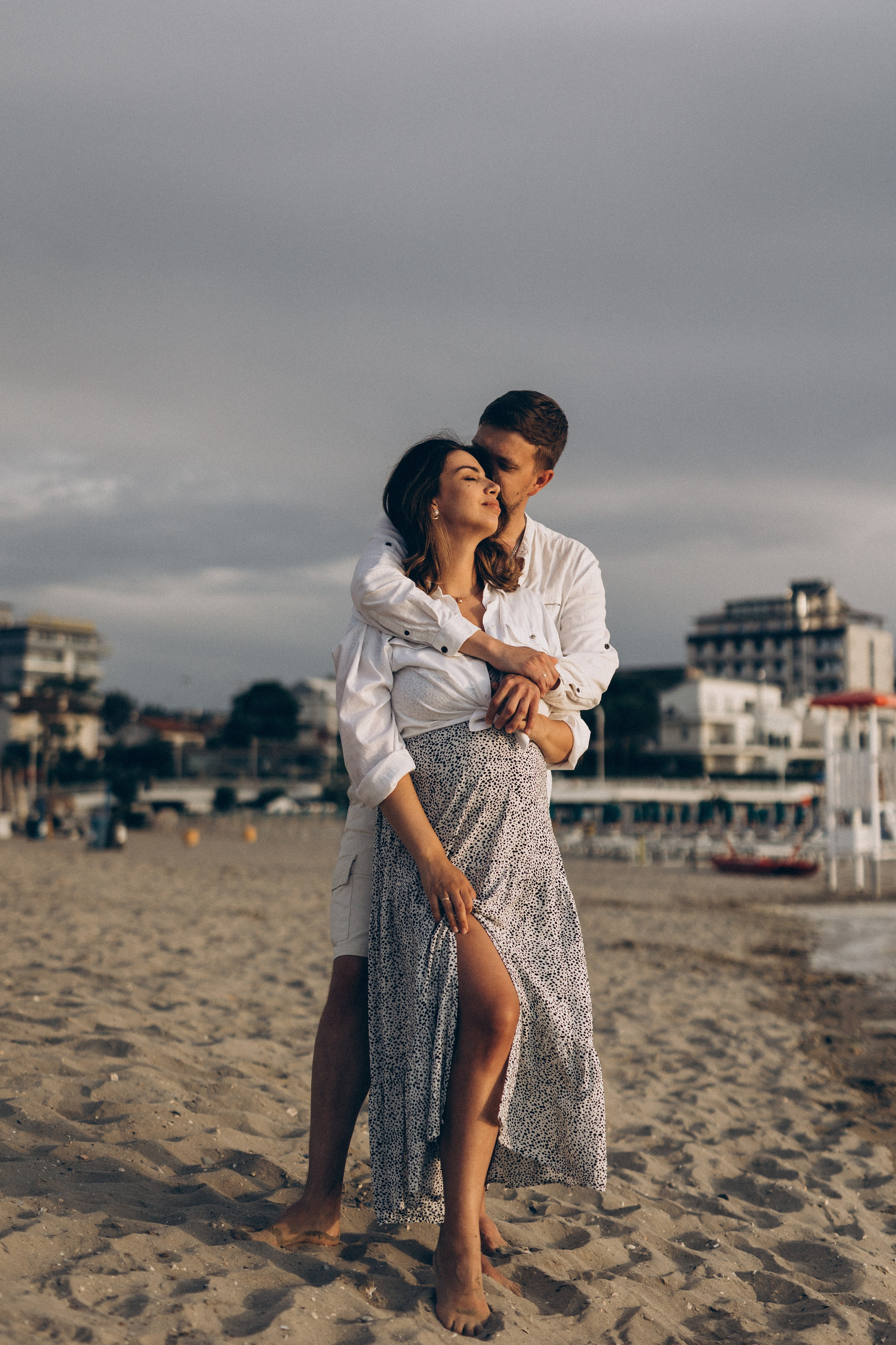 Donna incinta e il suo compagno si abbracciano sulla spiaggia in un’atmosfera intima
