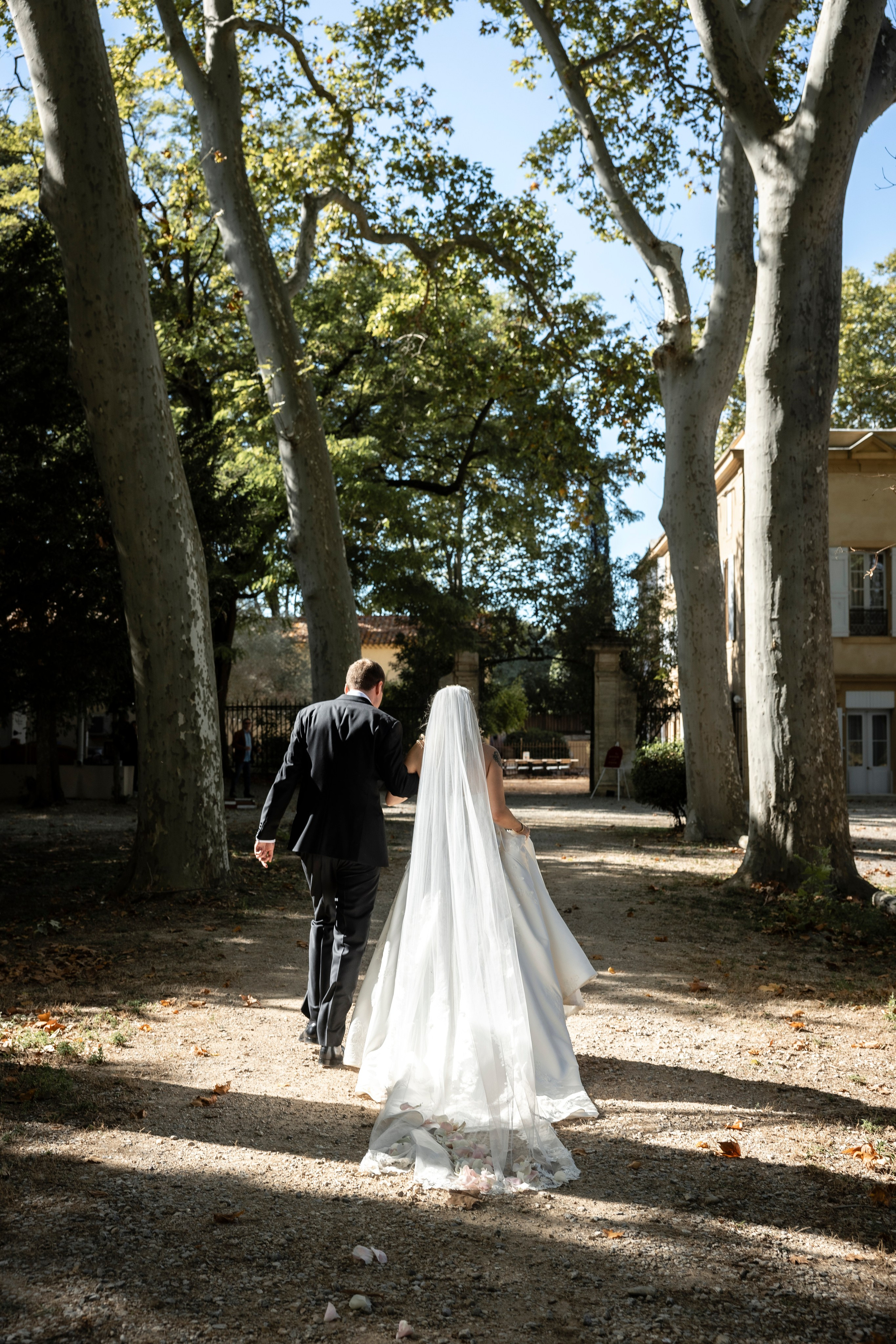 Les mariés marchant main dans la main sous les arbres du domaine du Château Rieutort après la cérémonie