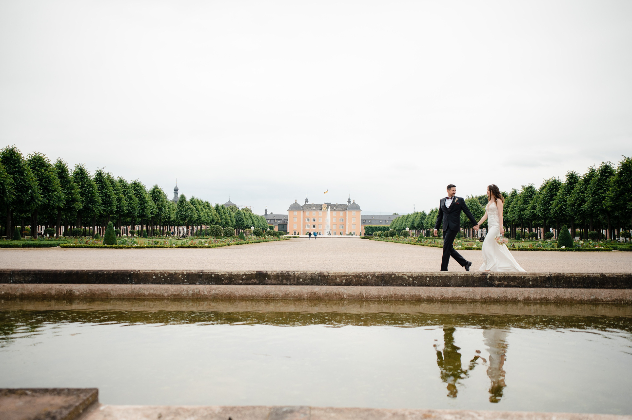 Brautpaar beim Spaziergang vor Schloss Schwetzingen mit Spiegelung im Wasser