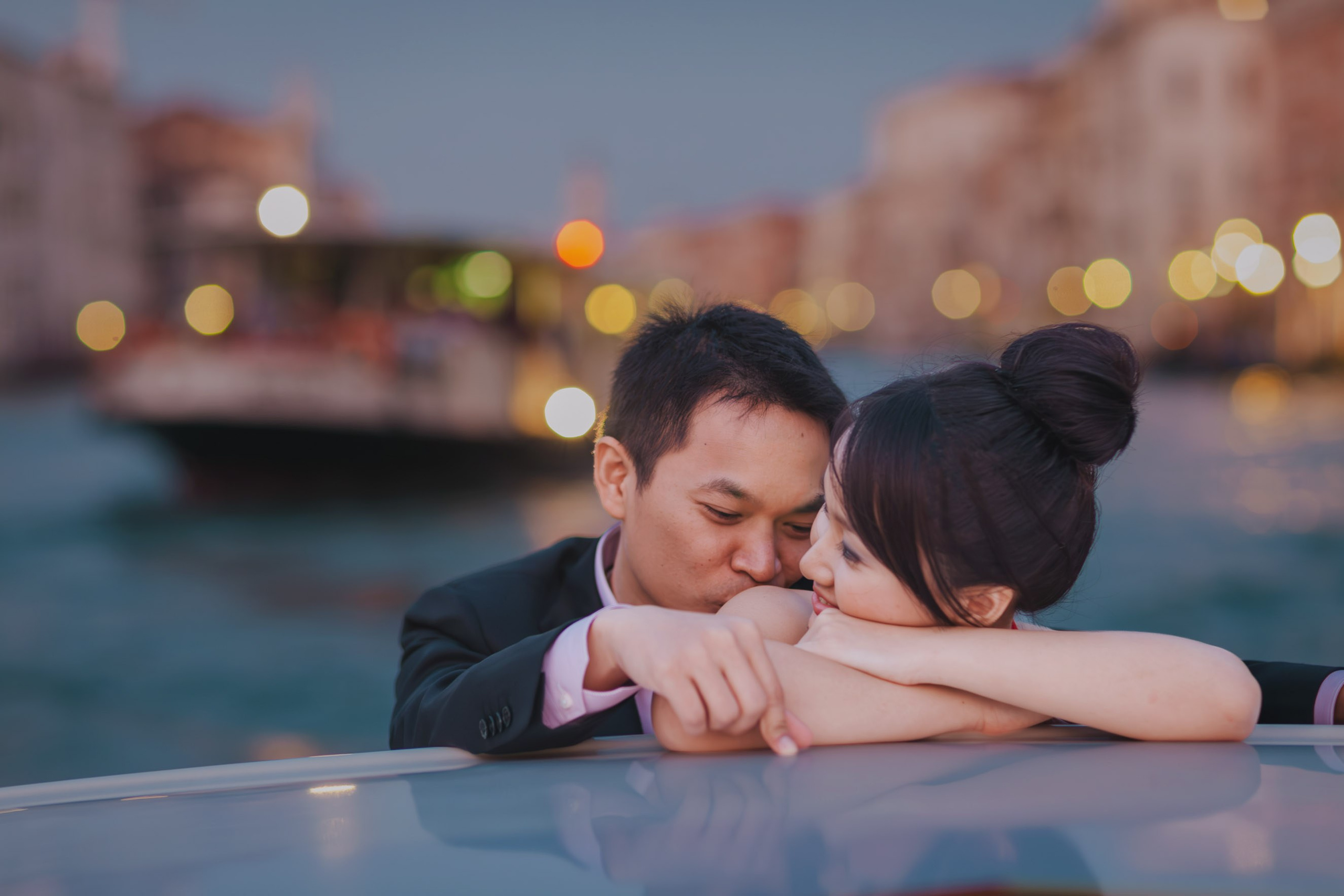 A young Thai couple snuggle up as they explore the historical canals of  Venice at Dusk in a private boat.