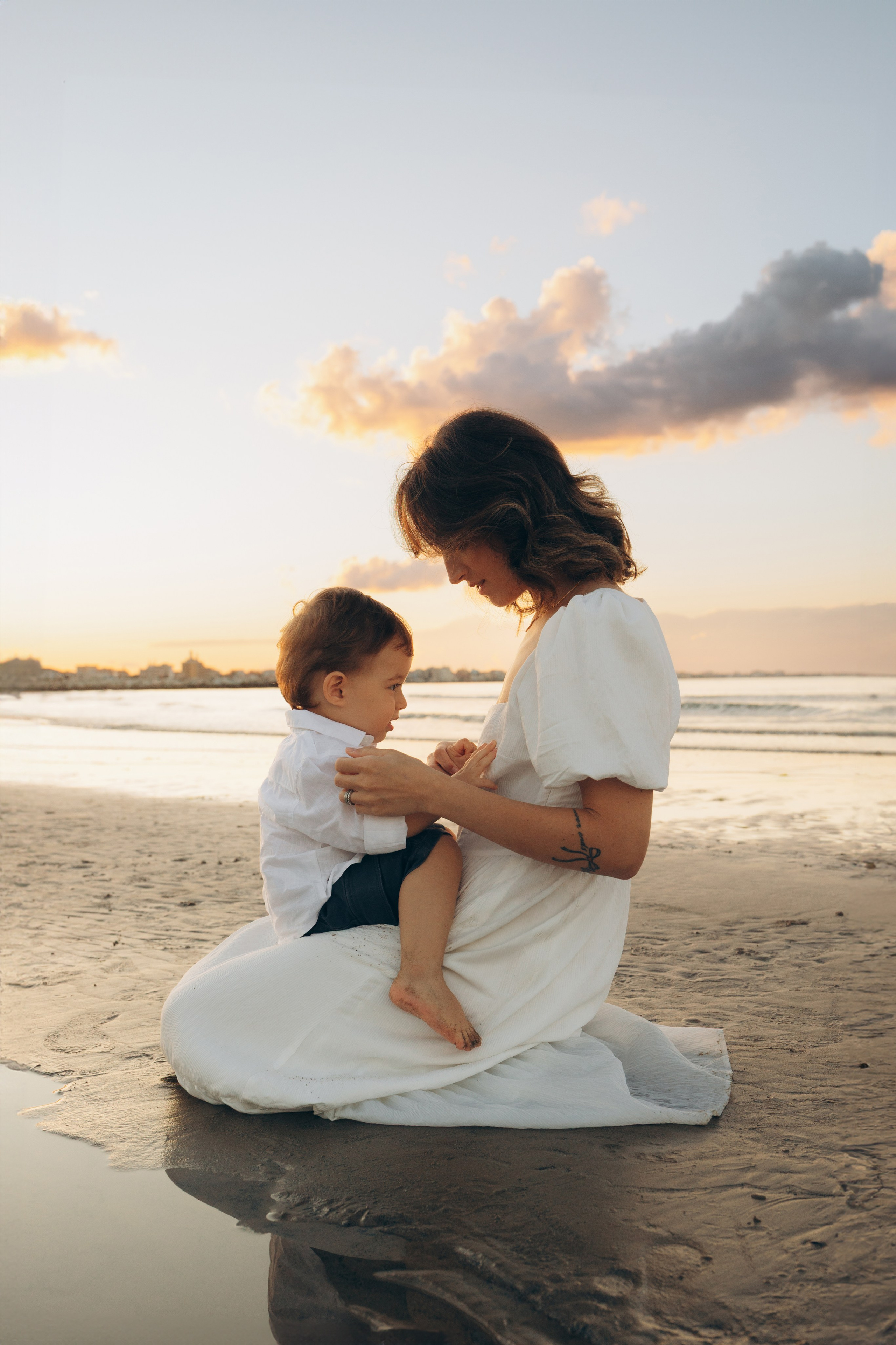 mamma seduta con bambino sulla spiaggia durante un servizio fotografico a Rimini con luce morbida