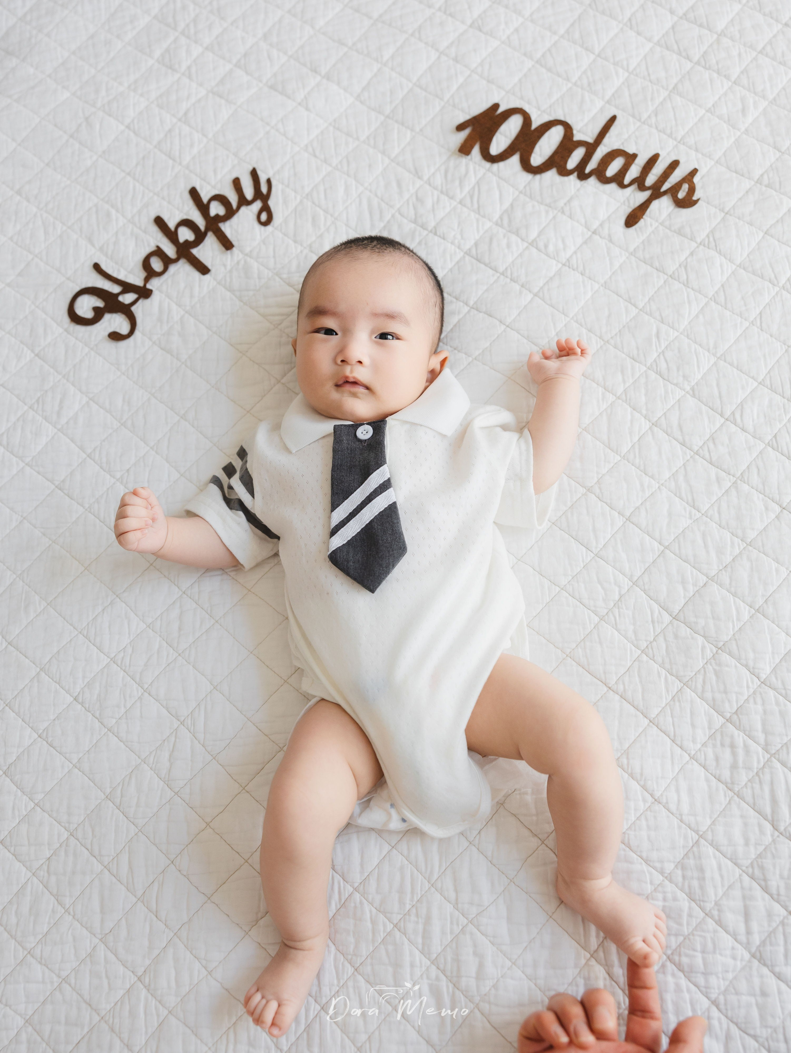 A 100-day-old baby lying on a white quilt for a simple milestone portrait at home.