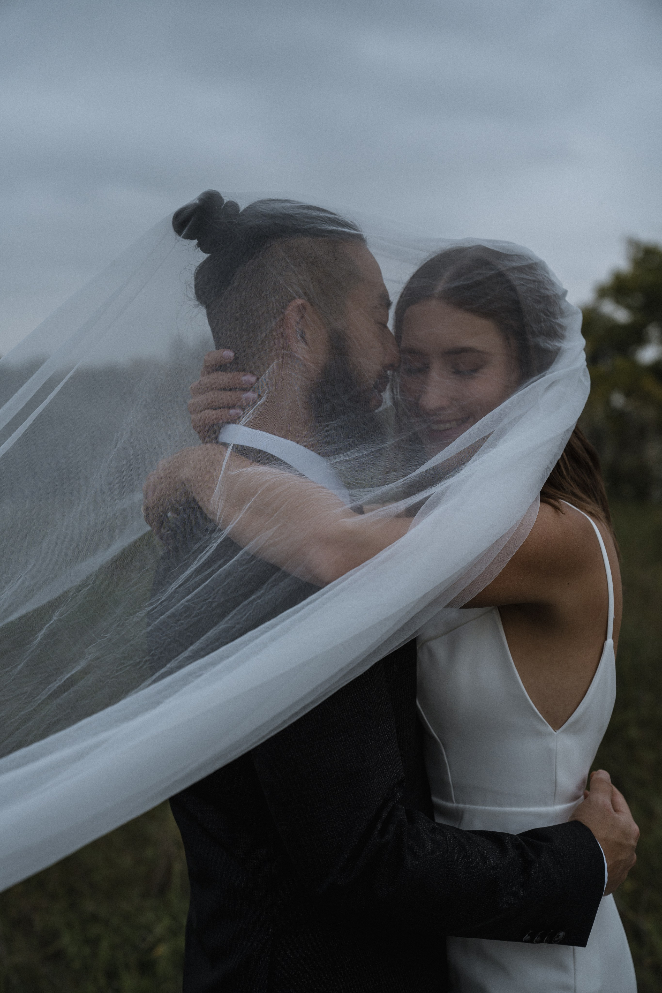 Bride hugging groom with their heads covered by the veil.
