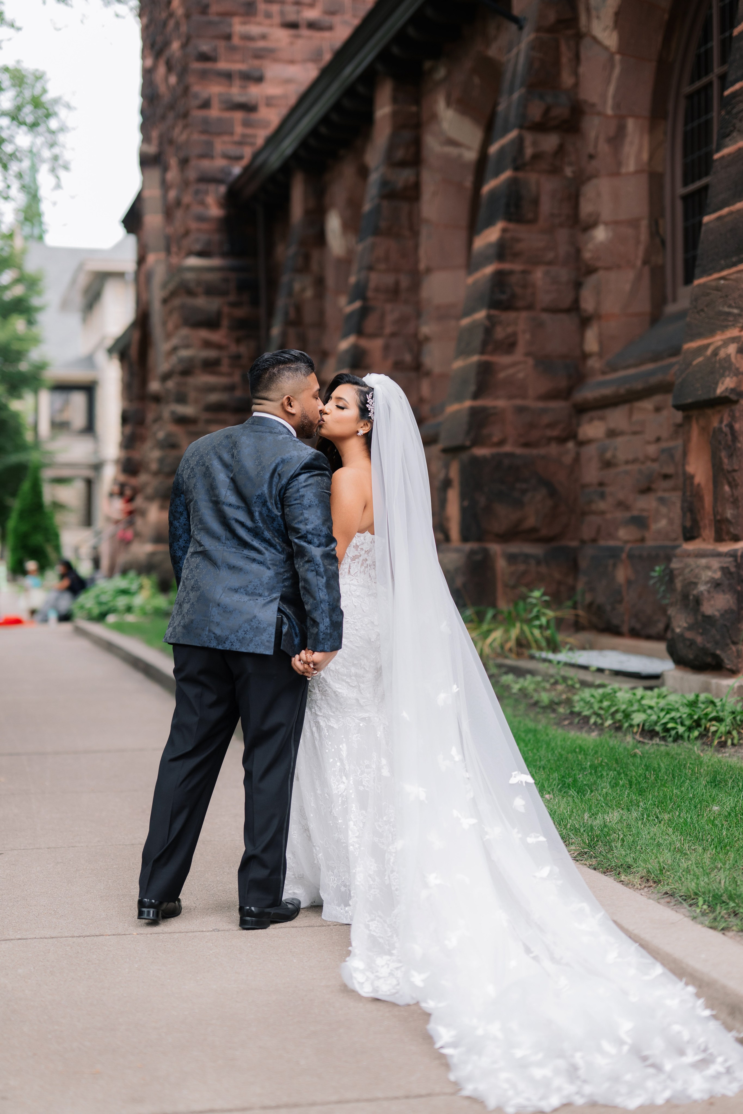 a bride and groom kissing on the sidewalk