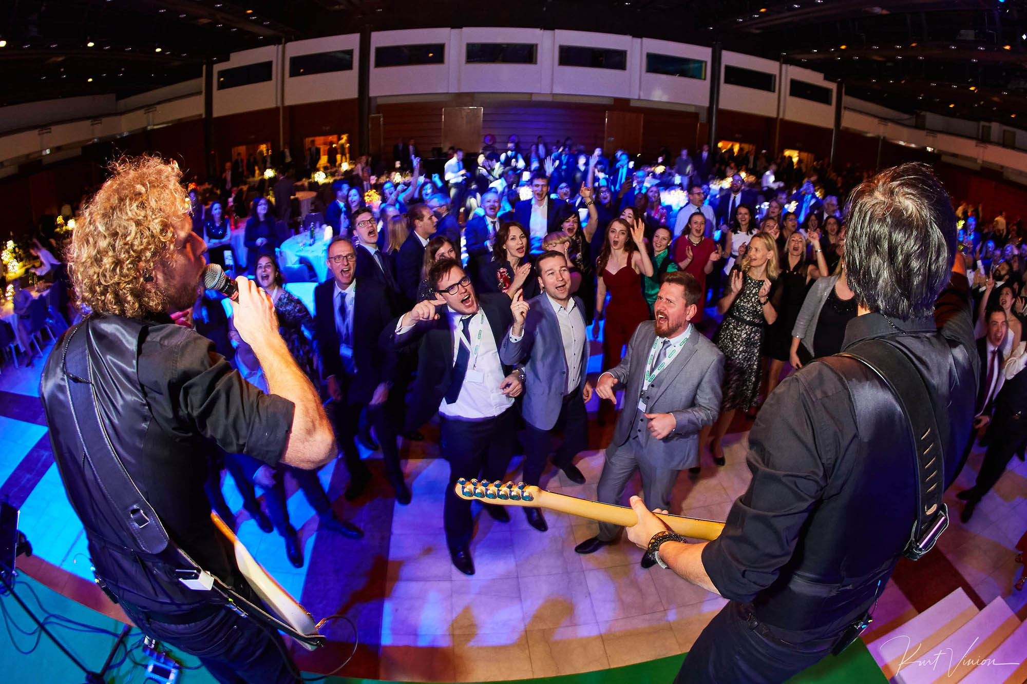 A crowd of businessmen pump their fists in the air as a rock band (in foreground) facing the crowd performs in Prague during a gala event.